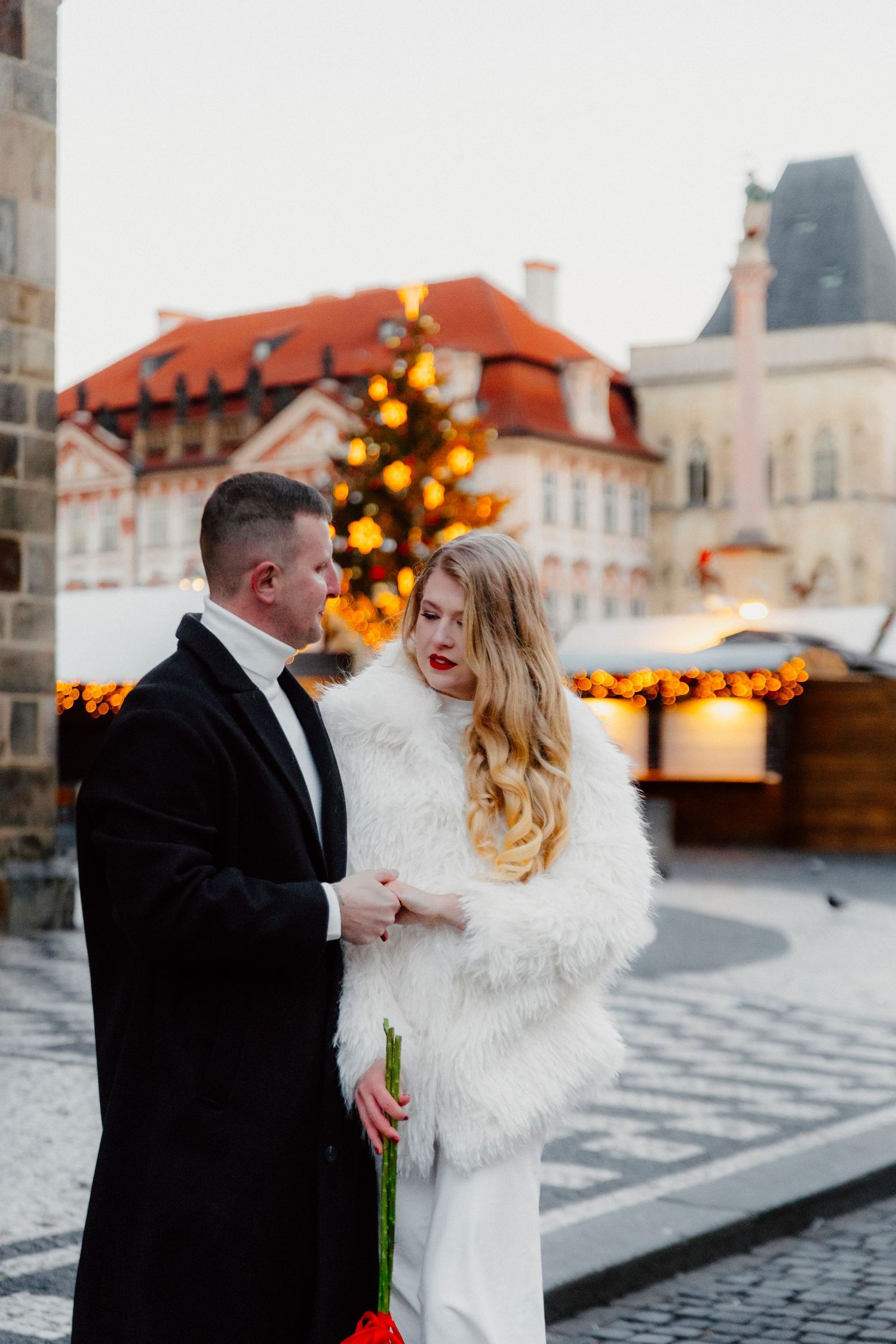 A winter wedding couple sharing an intimate moment in a European town square with festive lights.
