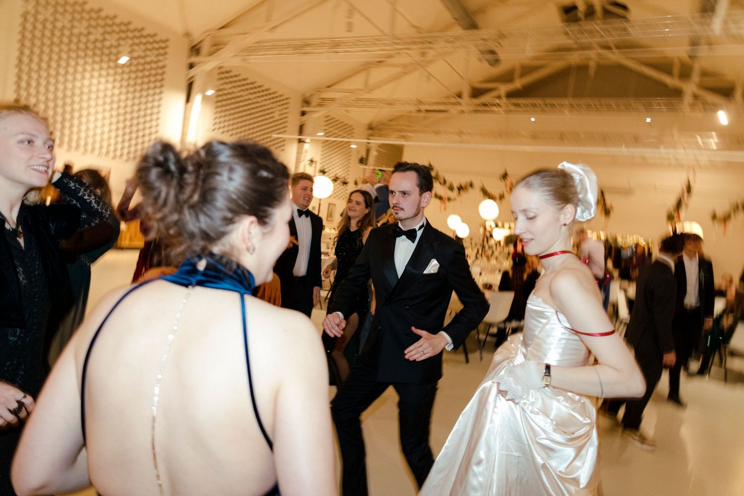 Wedding reception guests dancing and celebrating in a bright white venue space.