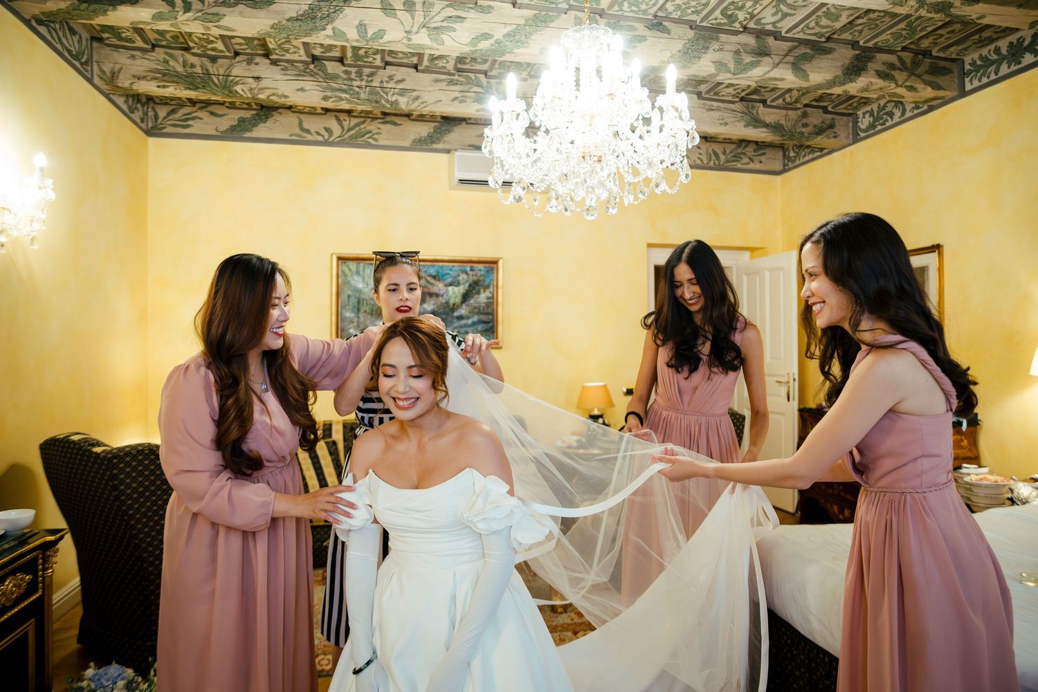 Wedding preparation scene with bridesmaids in pink dresses helping with final touches.