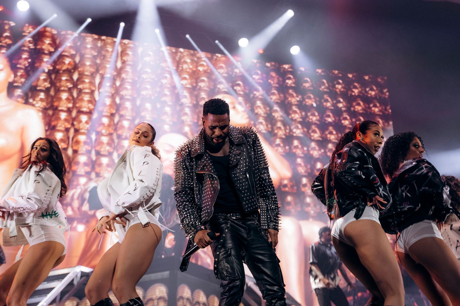 Concert performers on stage with dramatic lighting and backup dancers during an energetic live performance.