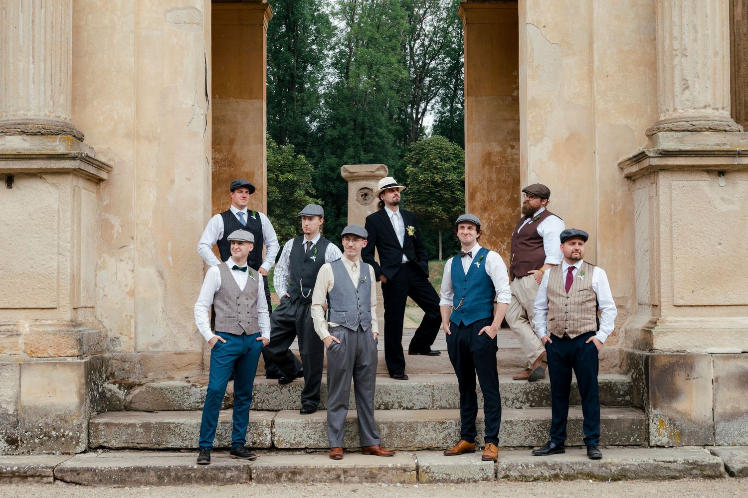 Group of men in vintage 1920s Peaky Blinders-style suits and flat caps posing on stone steps at historic venue.