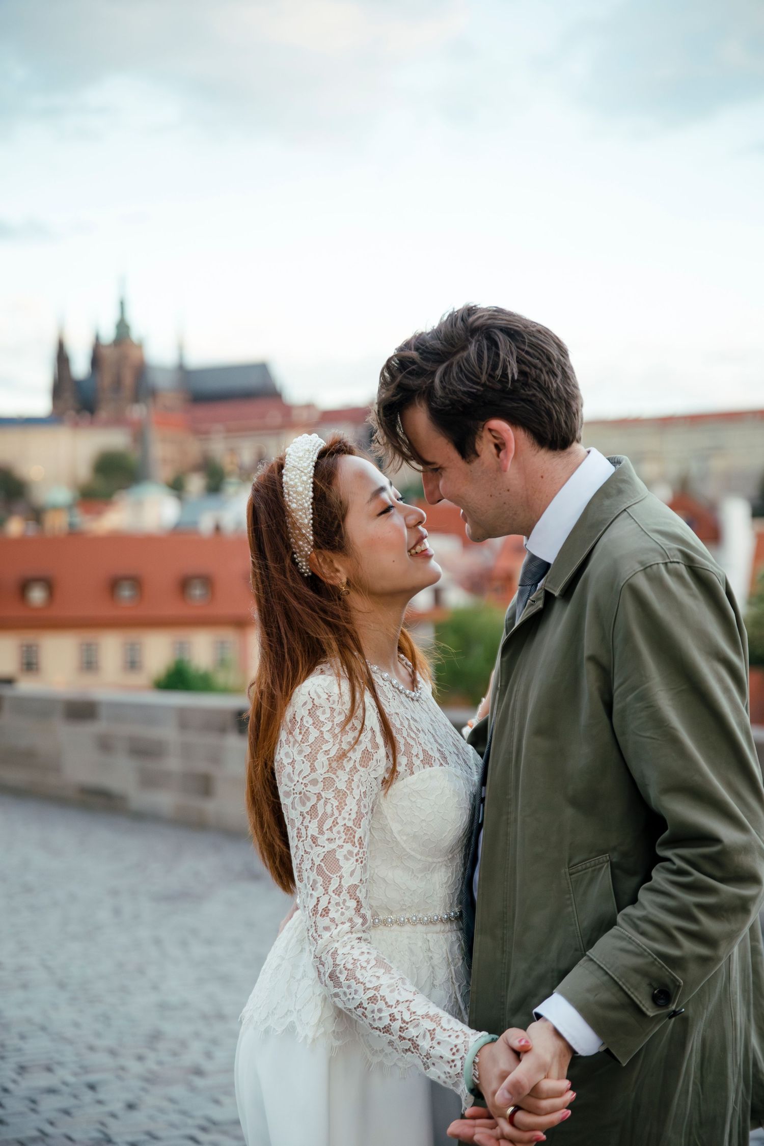 Couple shares intimate moment on Prague's historic bridge with castle views in background.