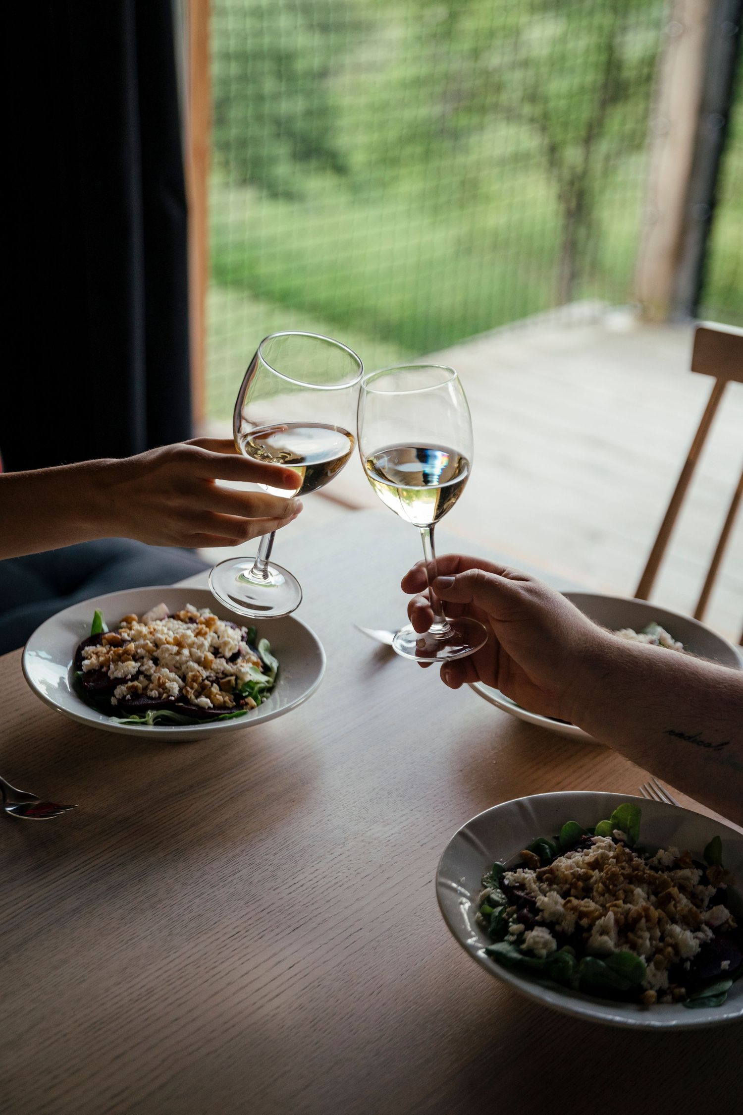 Two people enjoying wine and dinner at a table by a window with natural lighting.
