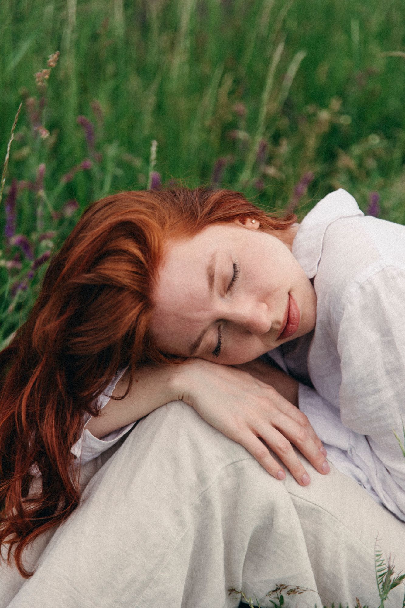 Person in white lying peacefully among wildflowers in green field.