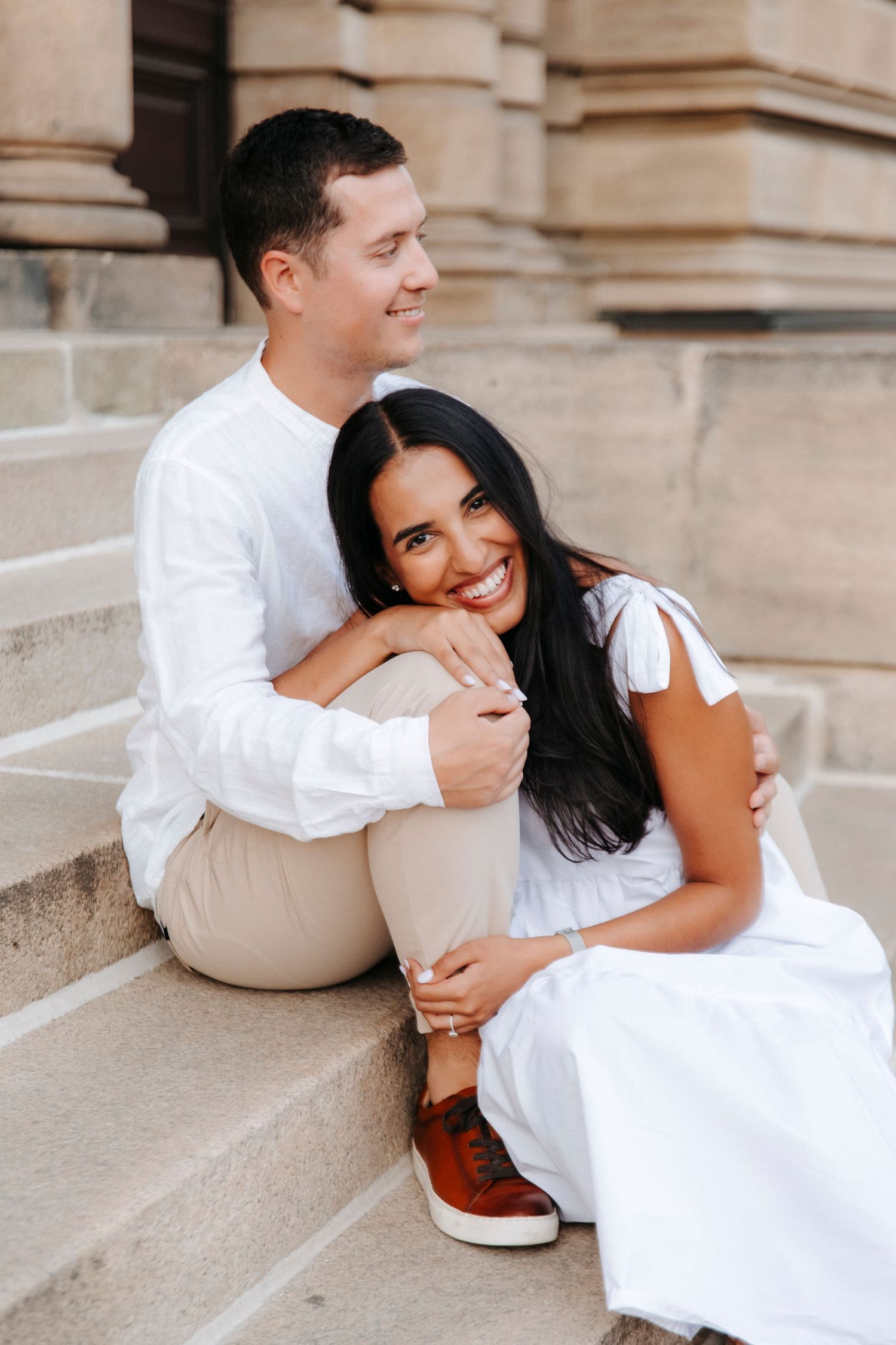Couple in light colored clothing embracing on architectural stone steps.