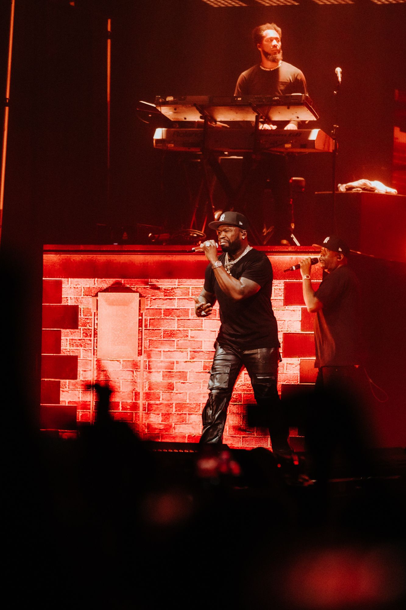 Concert performers on stage with red lighting and electronic equipment setup during a live music performance.