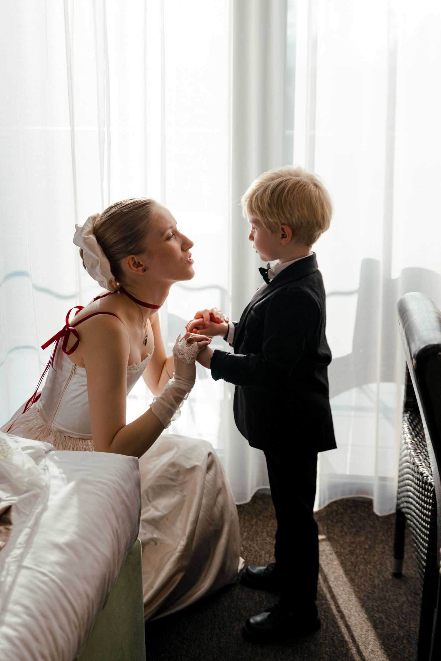 Sweet candid moment between a bride in white and young ring bearer in formal attire.