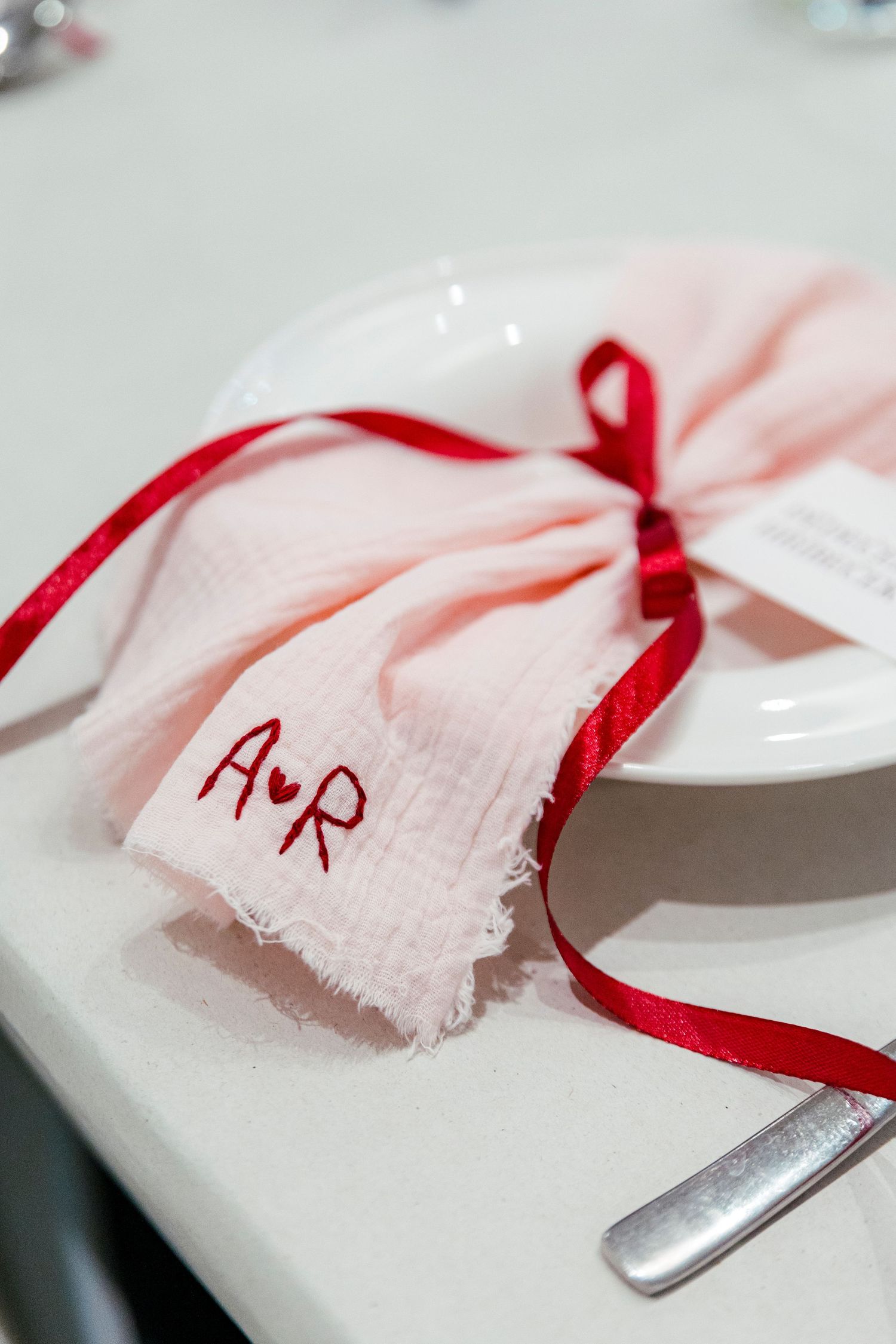 A red ribbon tied to a white cloth with handwritten text creates an artistic composition against a light background.