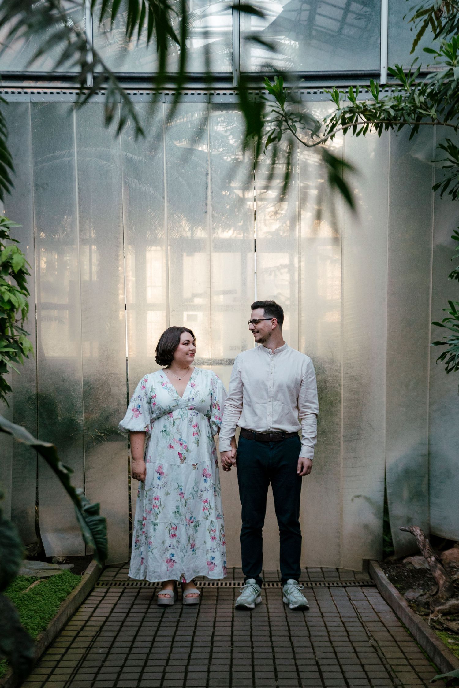 Couple walking through greenhouse with translucent walls and tropical plants.