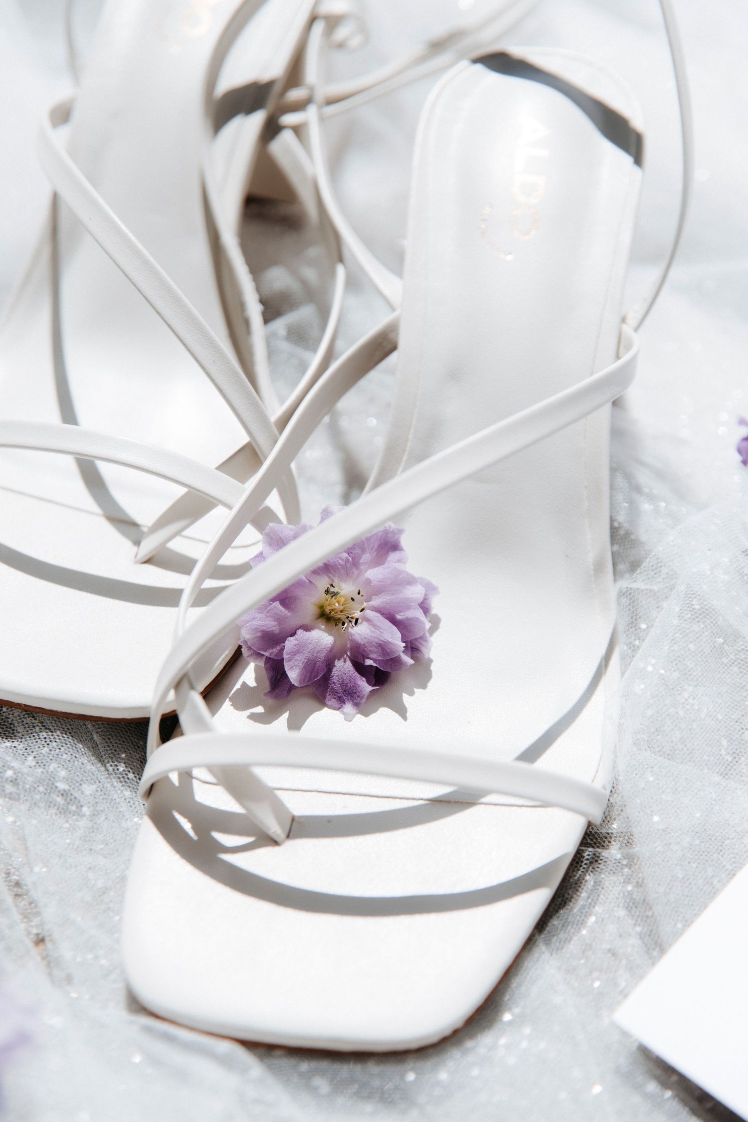 Elegant white bridal sandals adorned with a delicate purple flower detail.