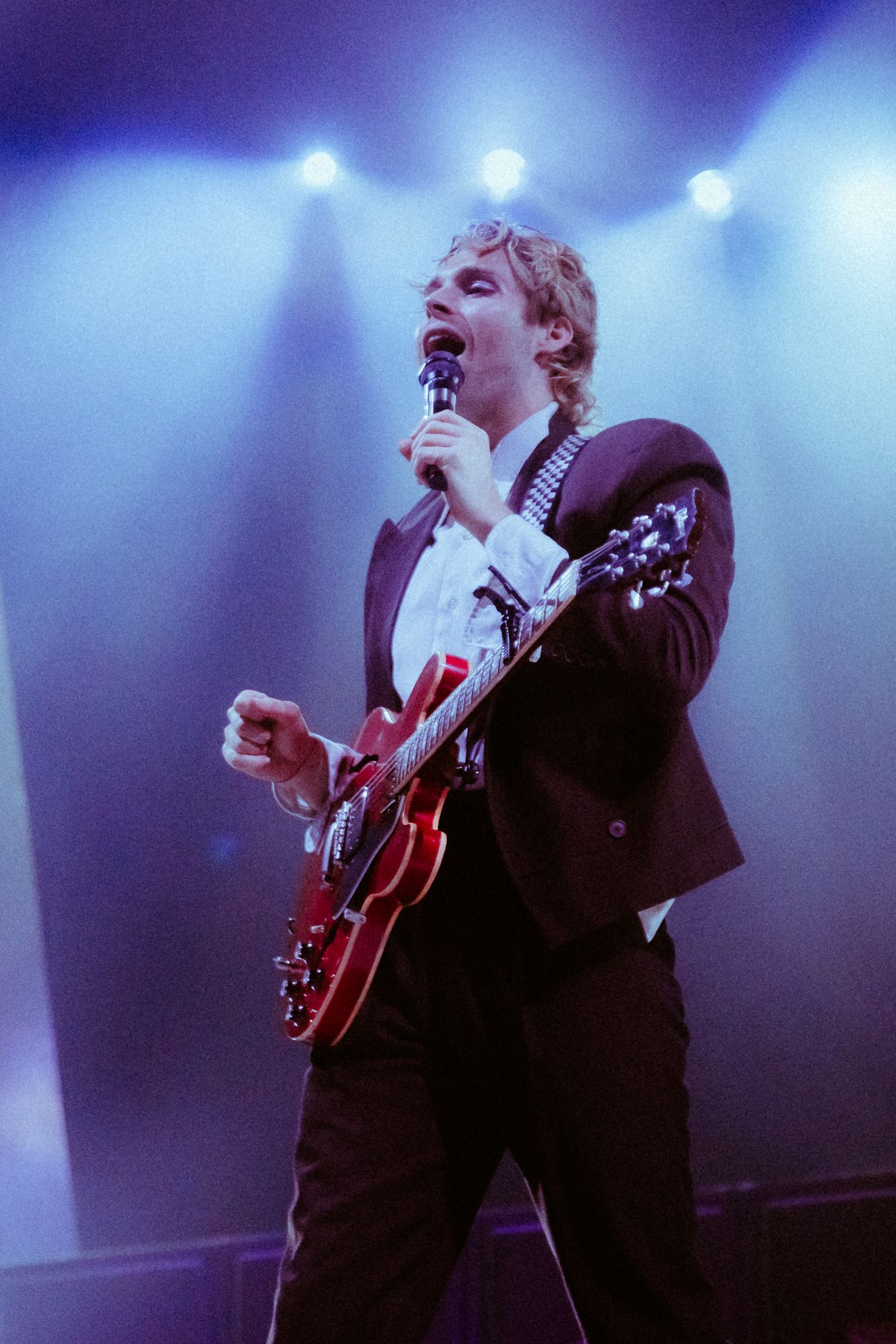 A guitarist performs on stage with dramatic blue lighting and fog effects during a concert performance.