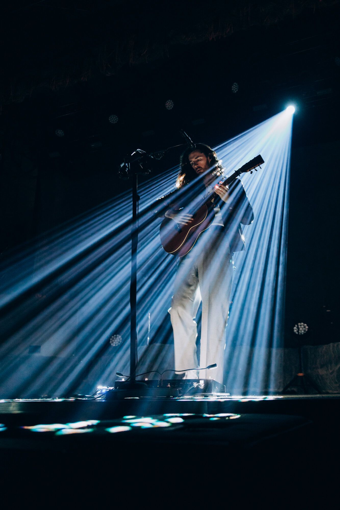 Dramatic stage lighting creates beams of white light cutting through darkness during a performance.