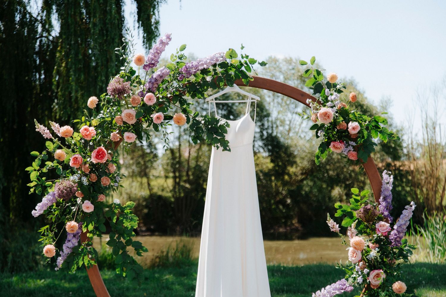 White wedding arch decorated with pink and purple roses against a bright blue sky.