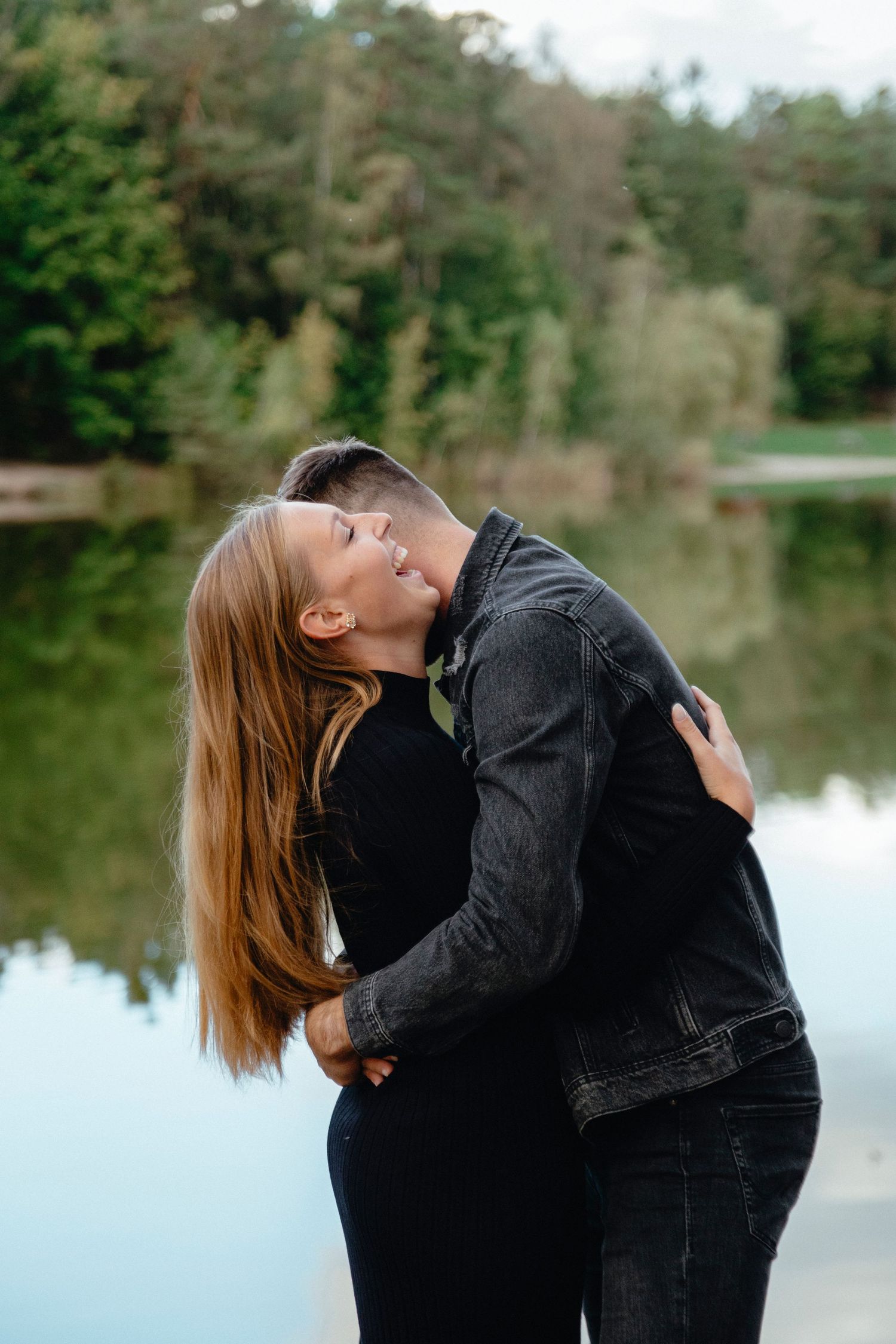 Romantic couple embraces by a serene lake during golden hour.