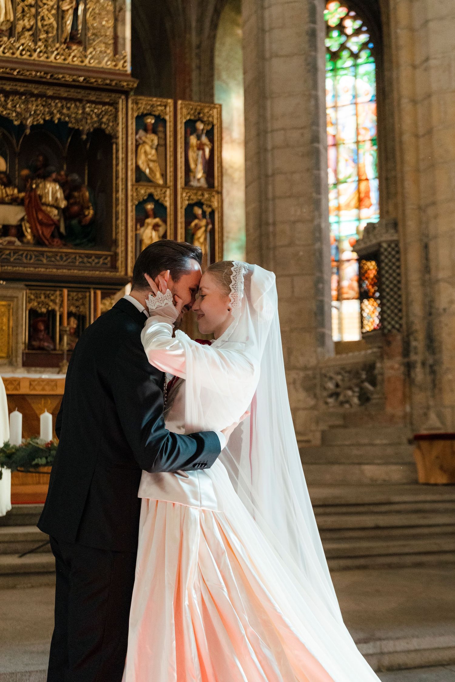 A romantic wedding kiss between a couple in a grand cathedral with ornate stained glass windows and stone architecture.