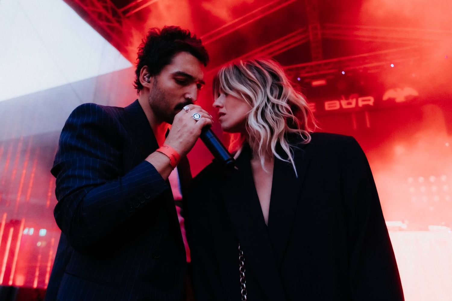 Couple in romantic embrace under dramatic red lighting at what appears to be a nightclub or party setting.