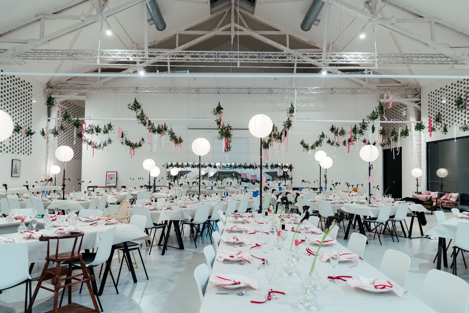 A modern white event space decorated with pink floral garlands and table settings for a celebration.
