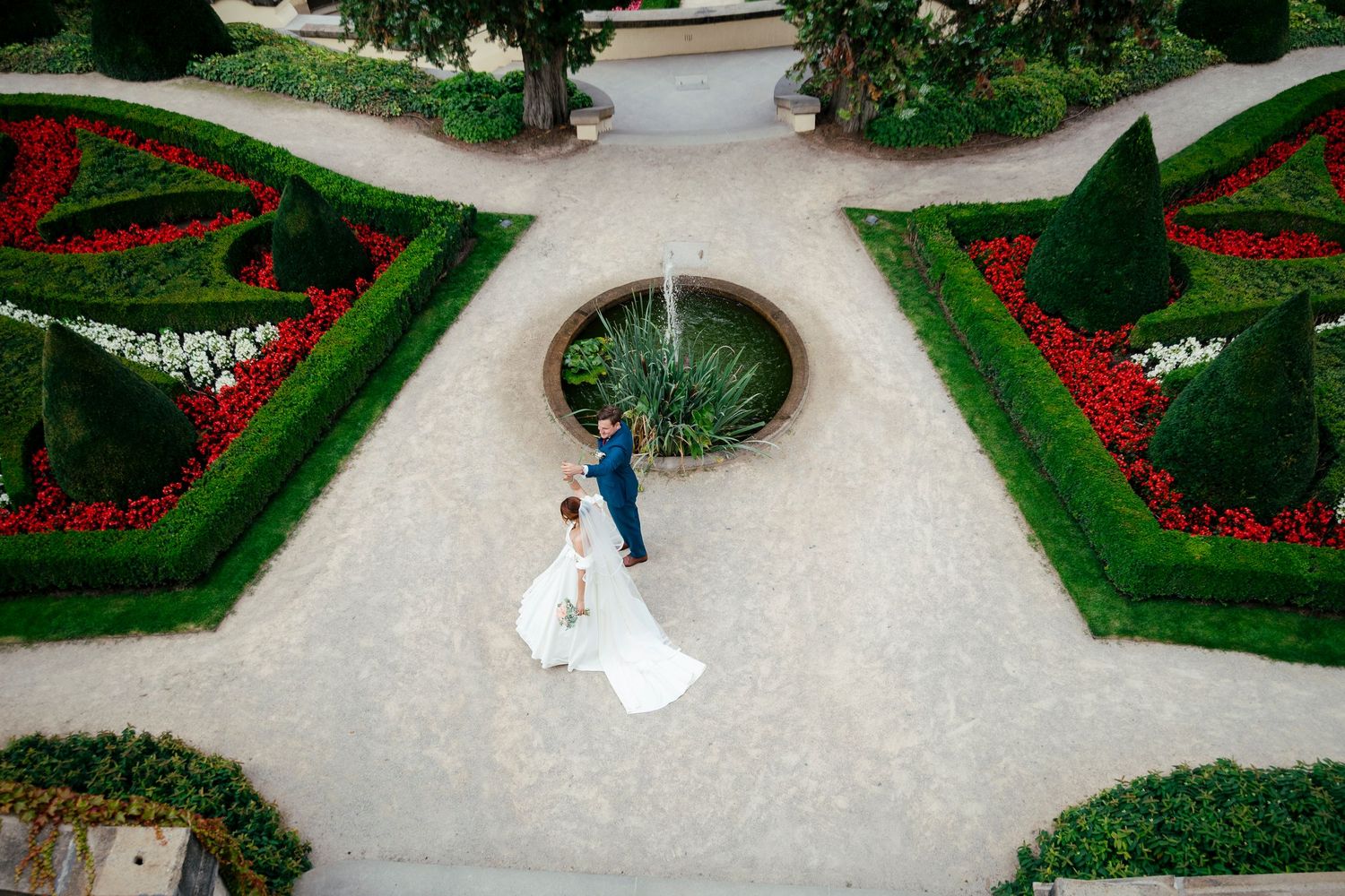 Aerial view of a garden wedding venue with manicured hedges and red flowers along winding pathways.