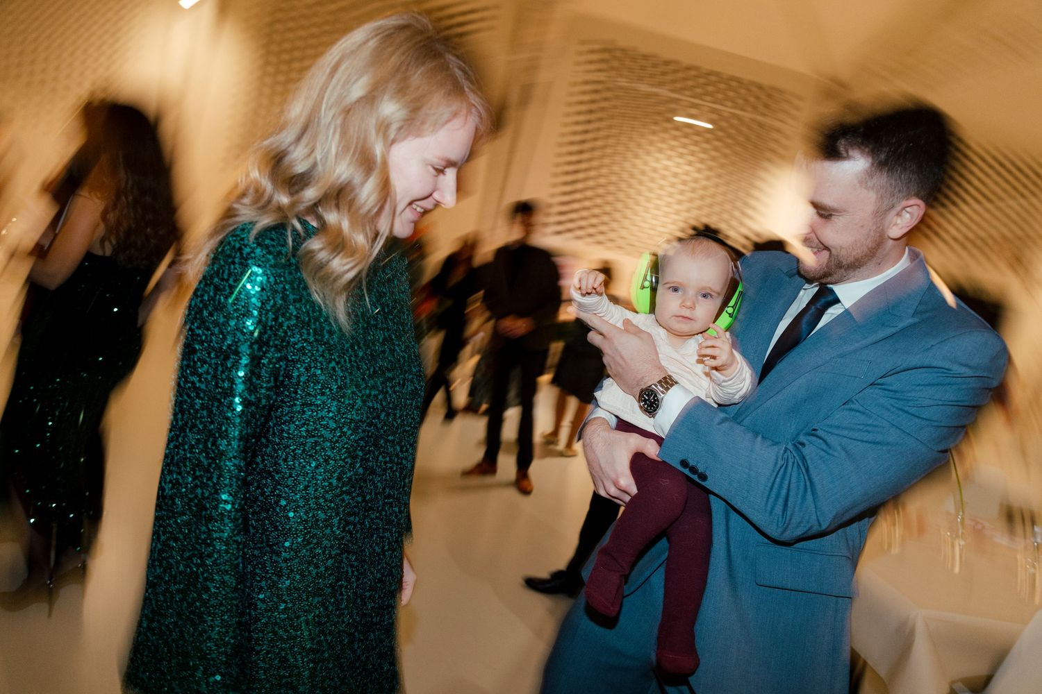 People gather at an event while someone in a blue suit holds a small baby.
