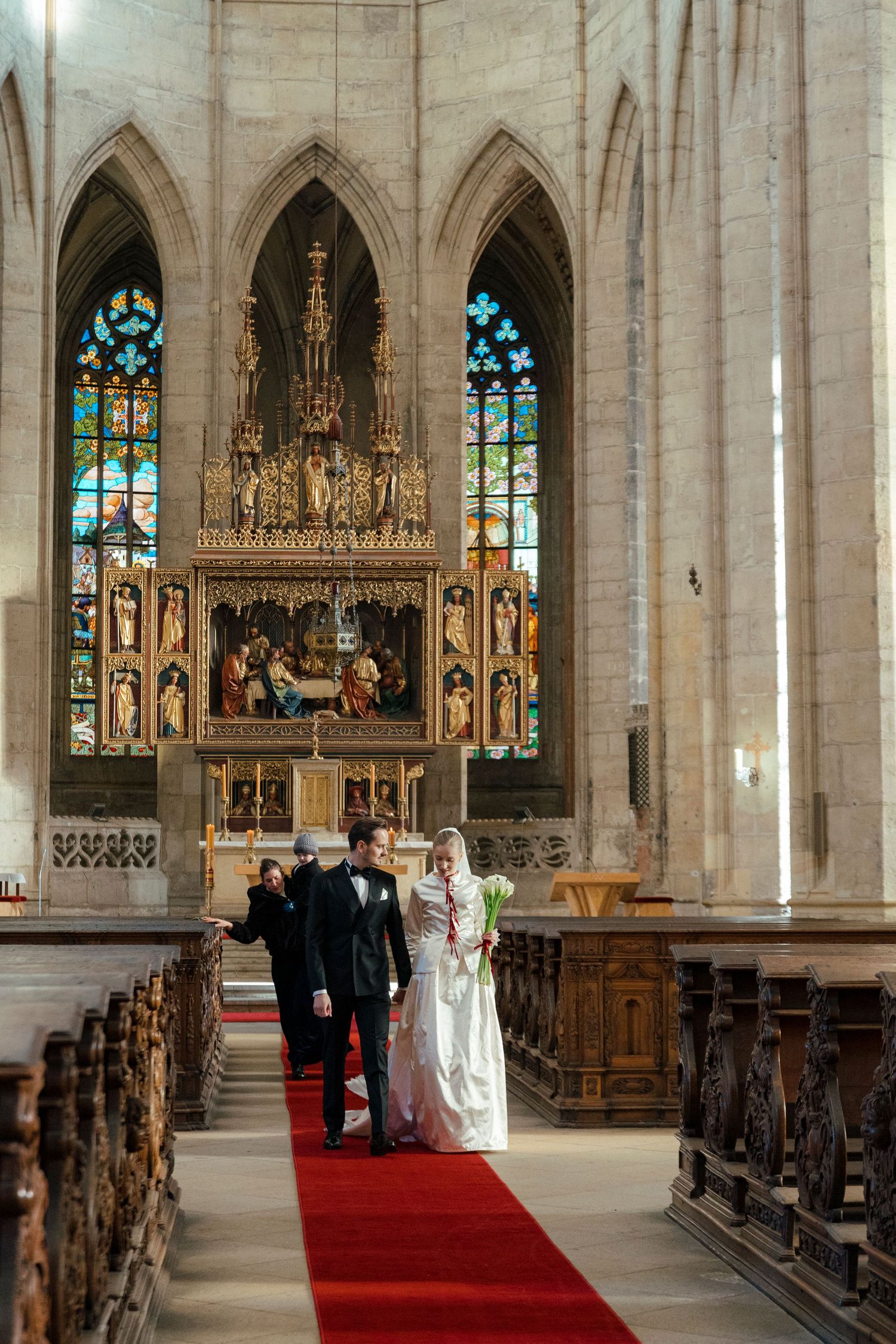 A wedding ceremony in a Gothic cathedral with stained glass windows and an ornate altar.