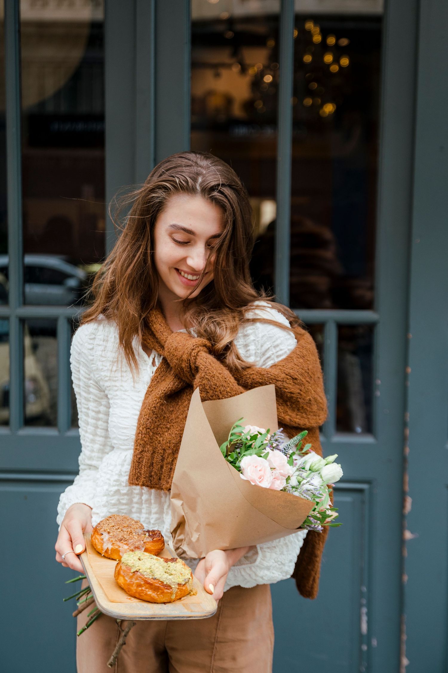 Person holding fresh pastries and flower bouquet wrapped in brown paper.