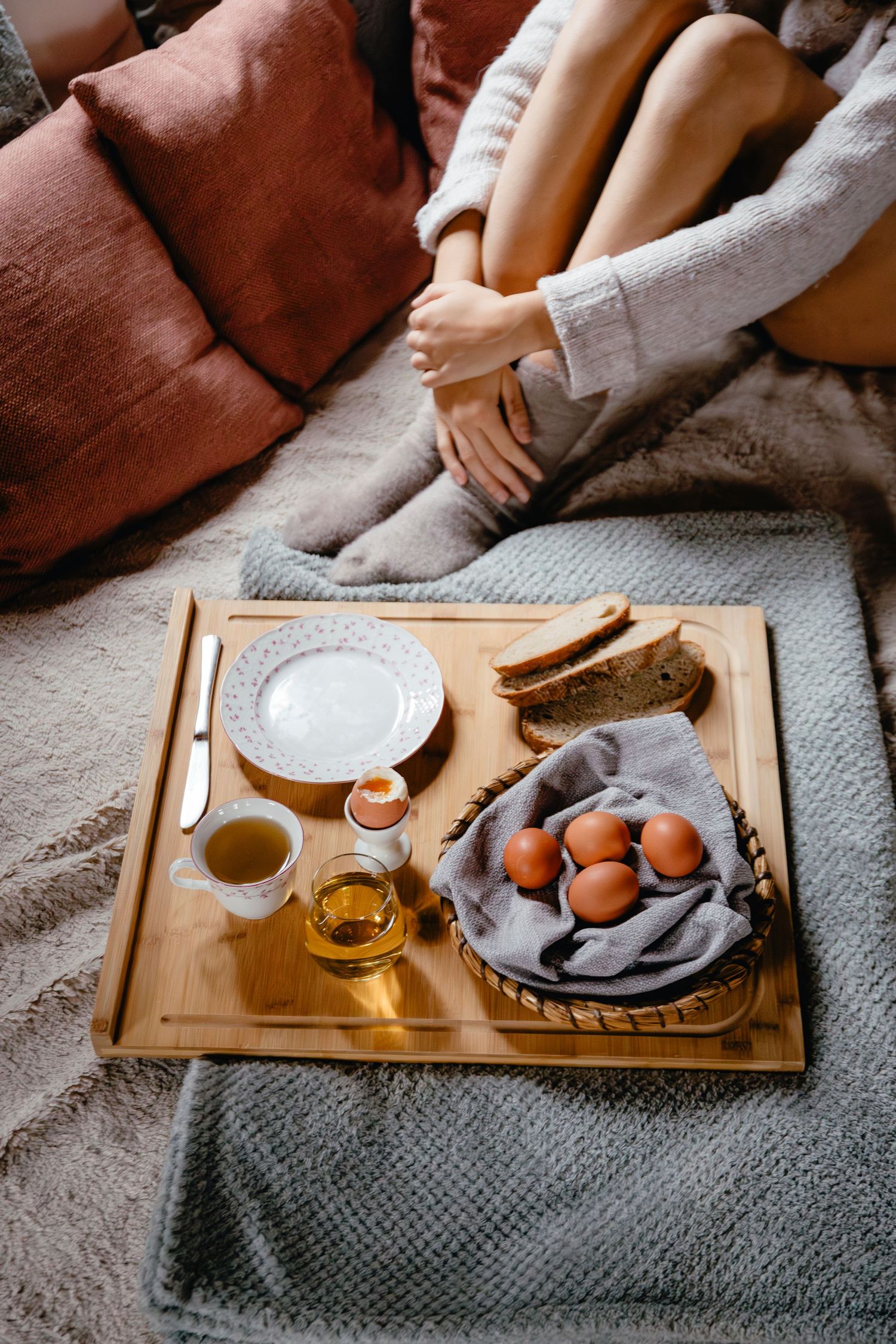 Wooden serving tray with eggs, honey, and plates on a cozy gray blanket.
