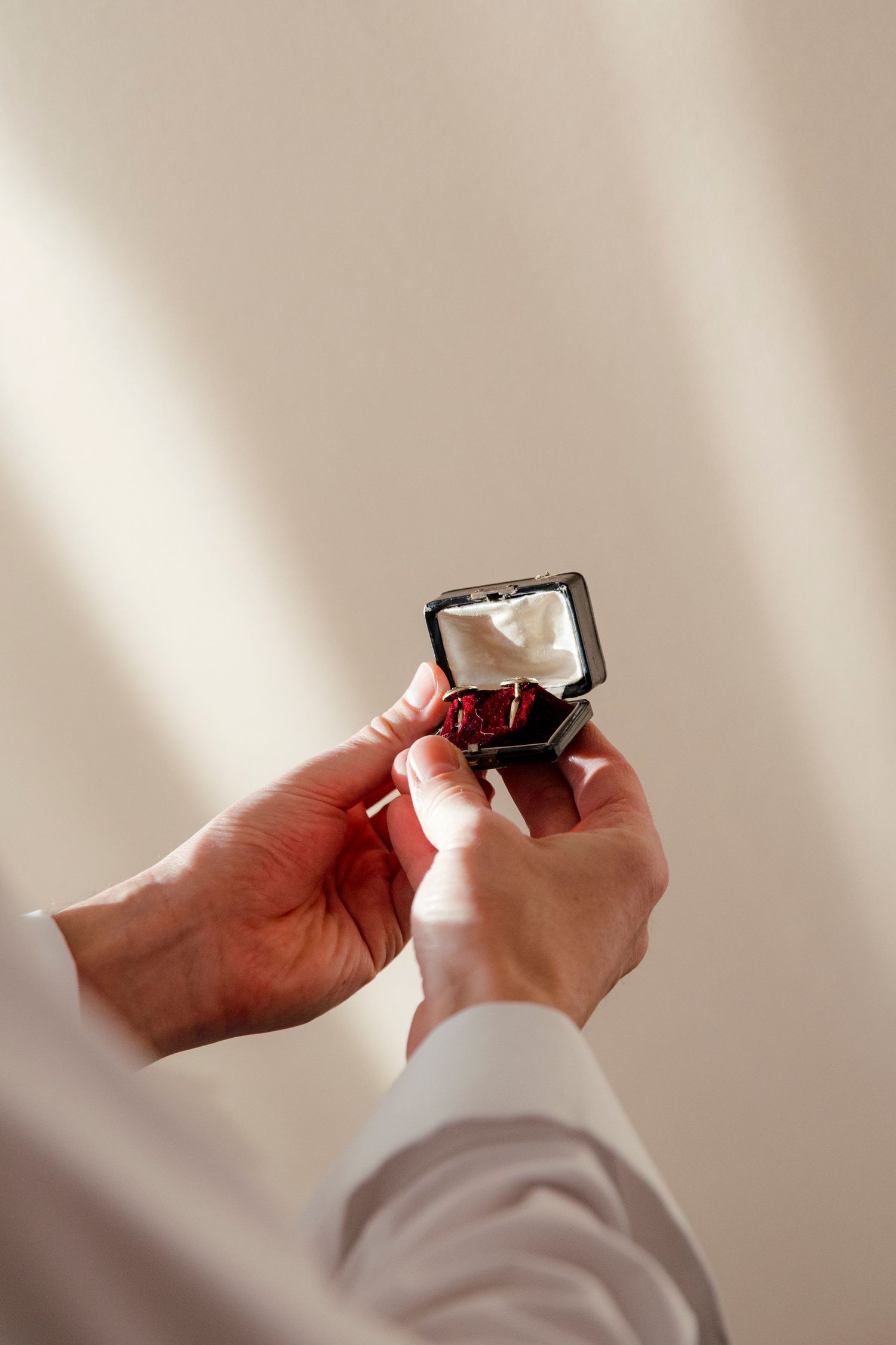 Hands holding and opening a small jewelry box in natural window light.