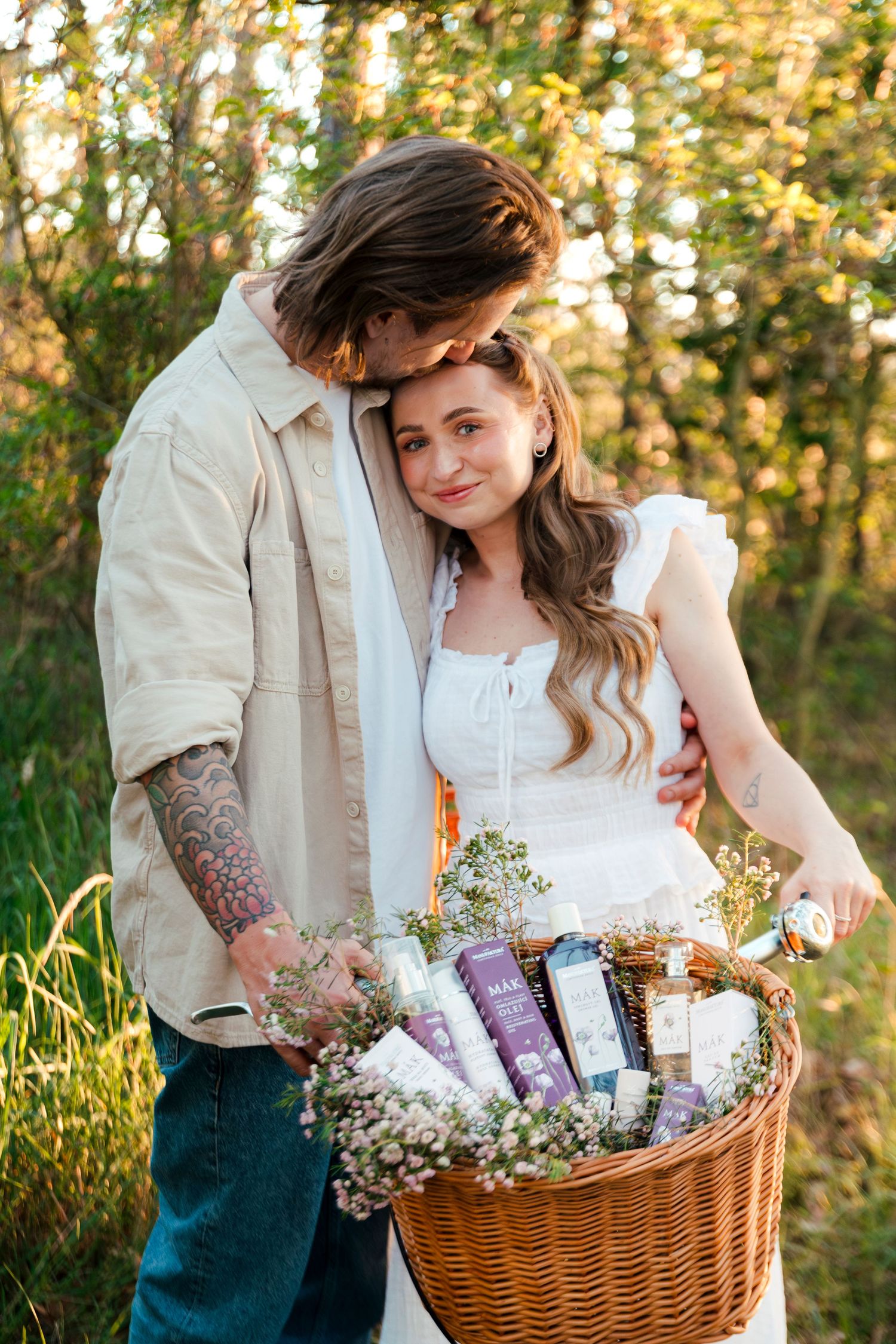 Couple embracing outdoors holding a wicker basket filled with lavender beauty products and wildflowers in golden sunlight.