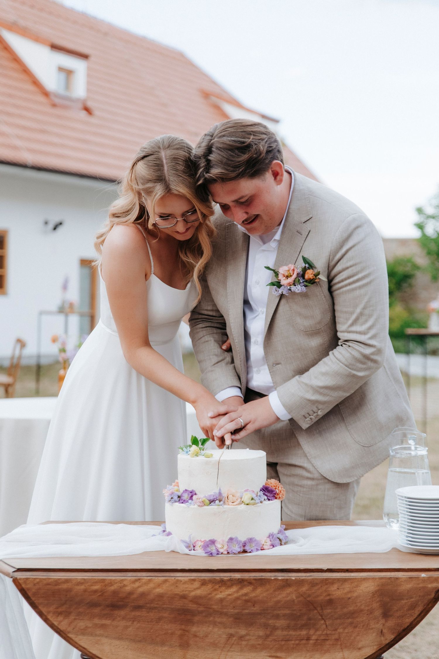 Newlyweds cut their two-tier white wedding cake decorated with purple flowers.