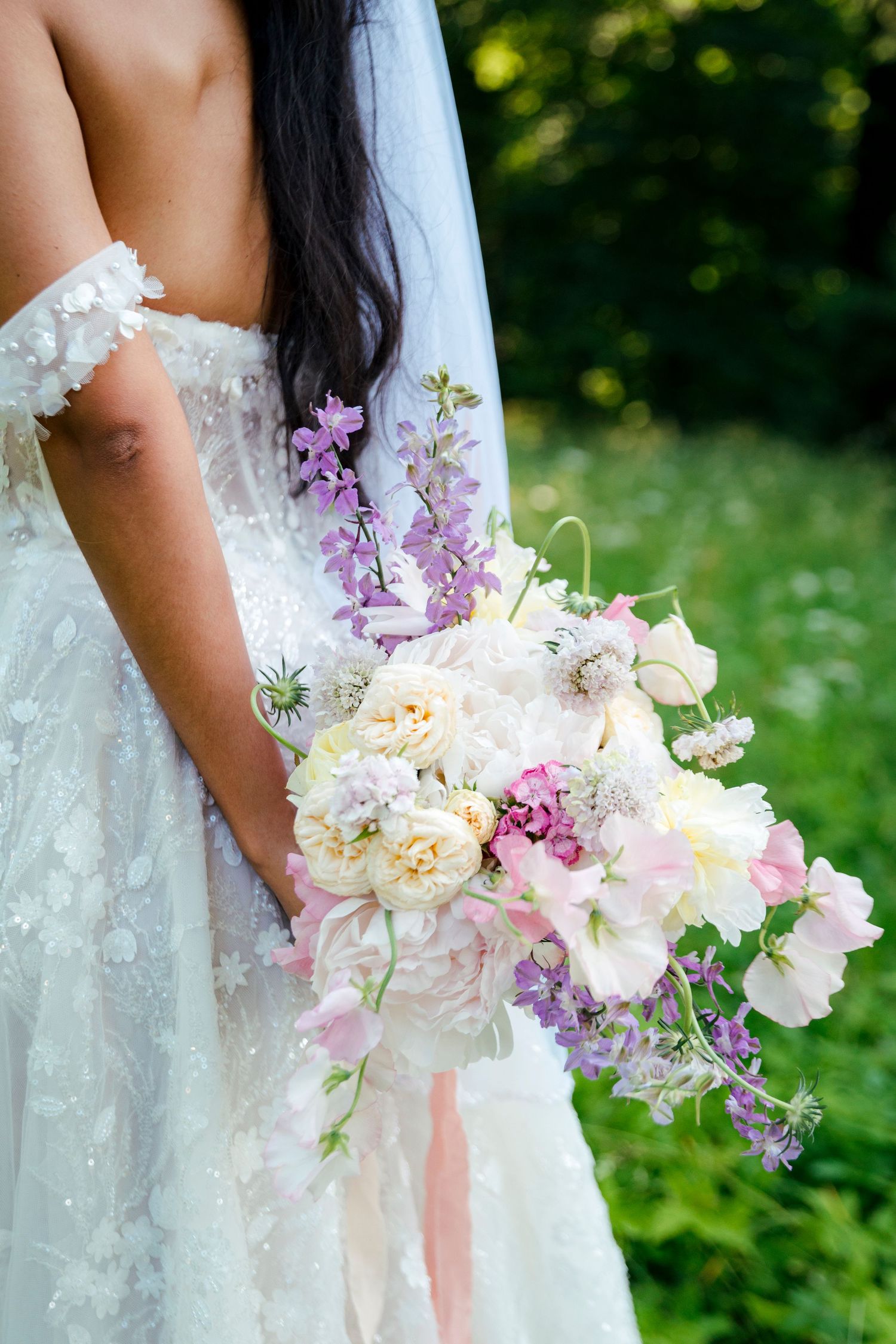 A delicate bridal bouquet features pink, purple, and white flowers with flowing ribbons.