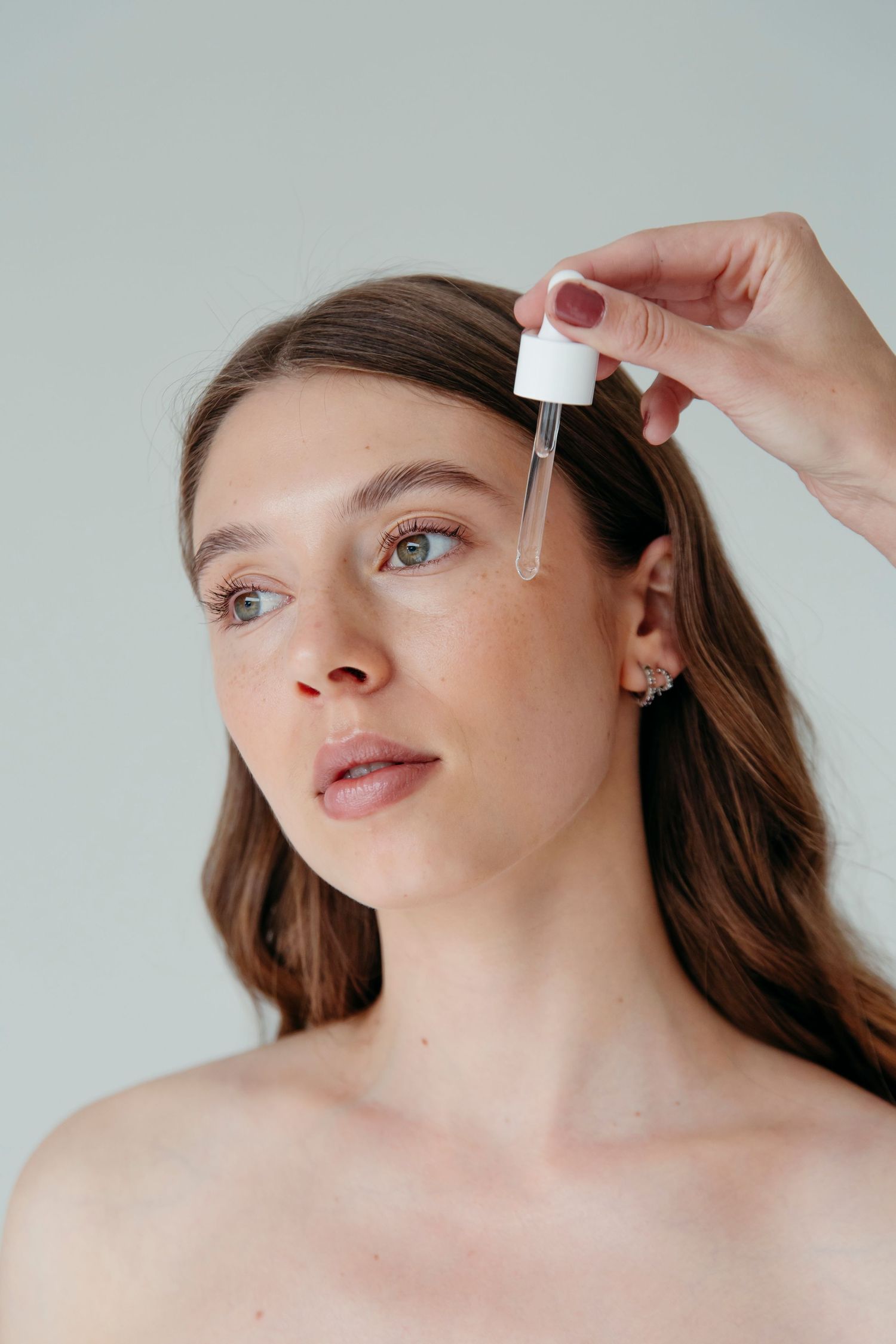 Beauty product demonstration showing application of skincare serum dropper.