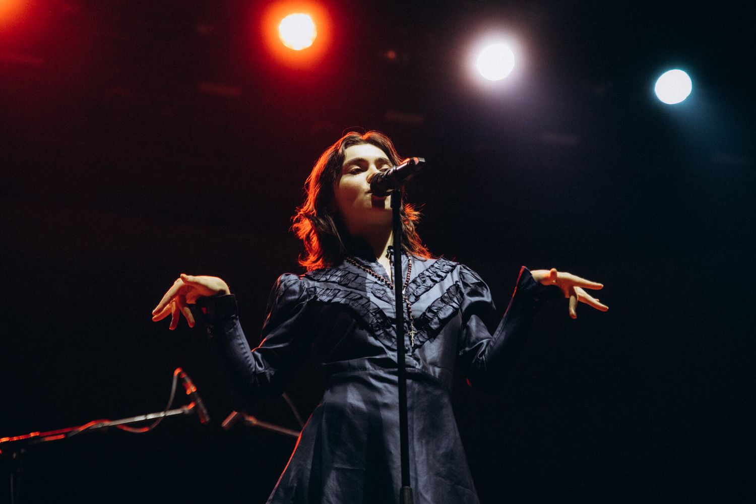 Concert performer silhouetted against dramatic red and blue stage lighting during live music performance.