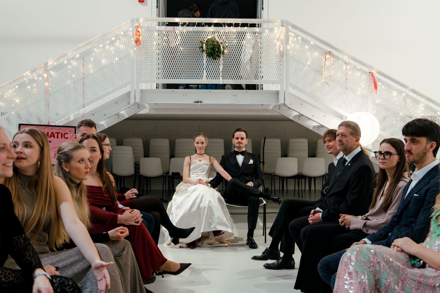 Wedding celebration in a bright indoor venue with white walls and decorative lighting.