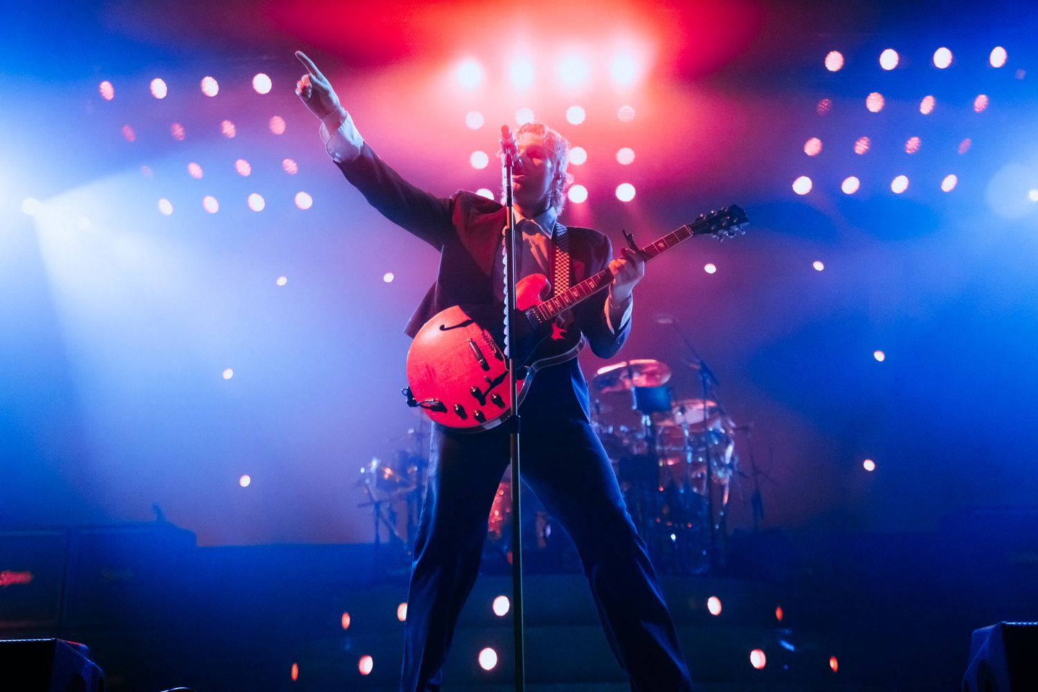 Concert performers on stage with dramatic red and blue lighting effects during a live music performance.