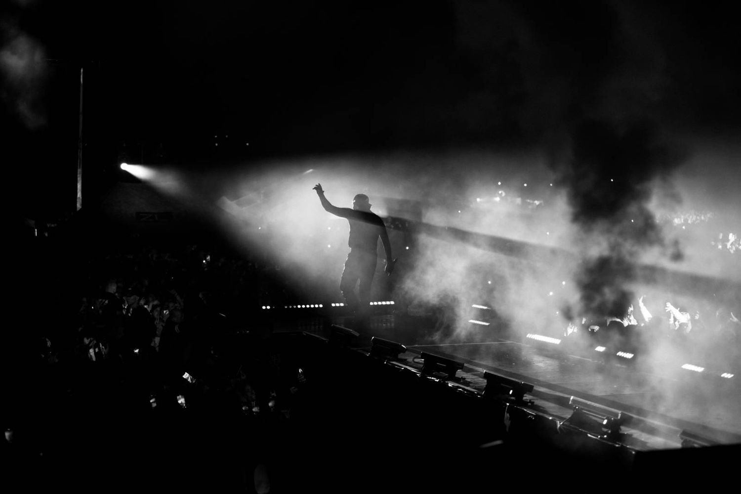 Black and white concert photo showing silhouettes of performers through atmospheric stage fog.
