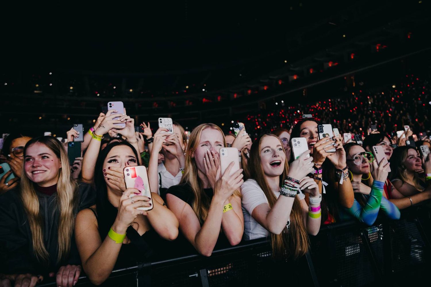 Concert crowd holds up glowing phones in darkened arena during live music performance.