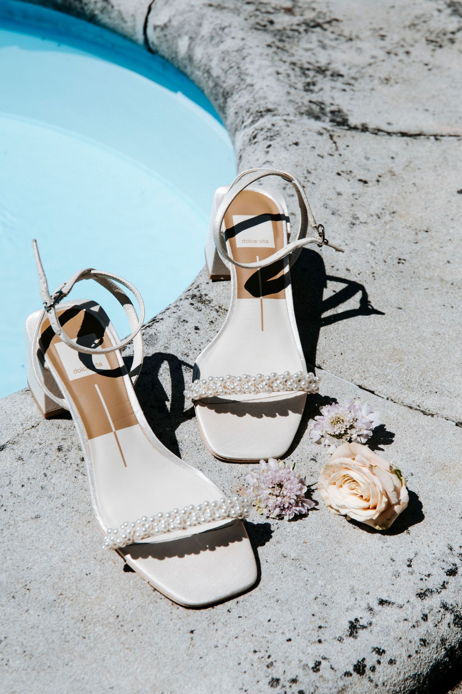 Elegant white and black bridal sandals displayed against a light blue background.