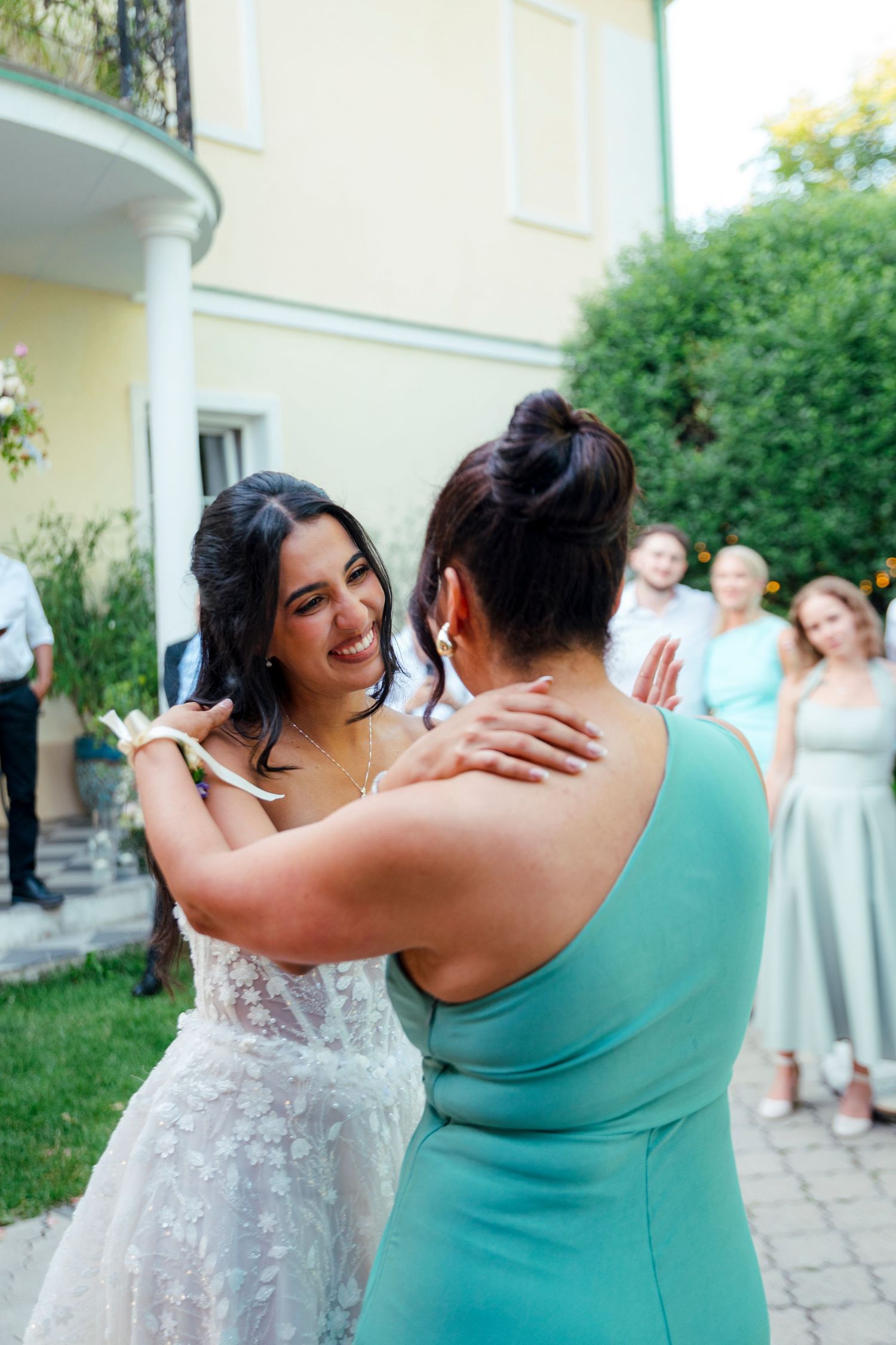 Wedding guests in turquoise dresses share emotional embraces during outdoor celebrations.
