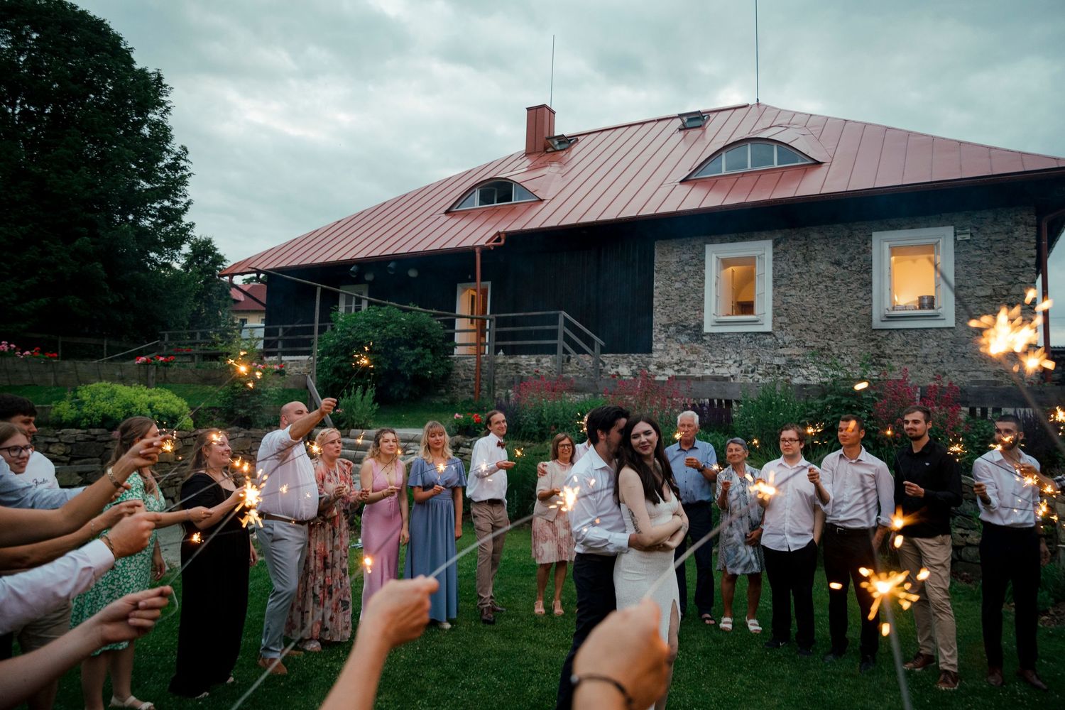 Wedding guests gather outside a rustic stone building at dusk for outdoor celebrations.