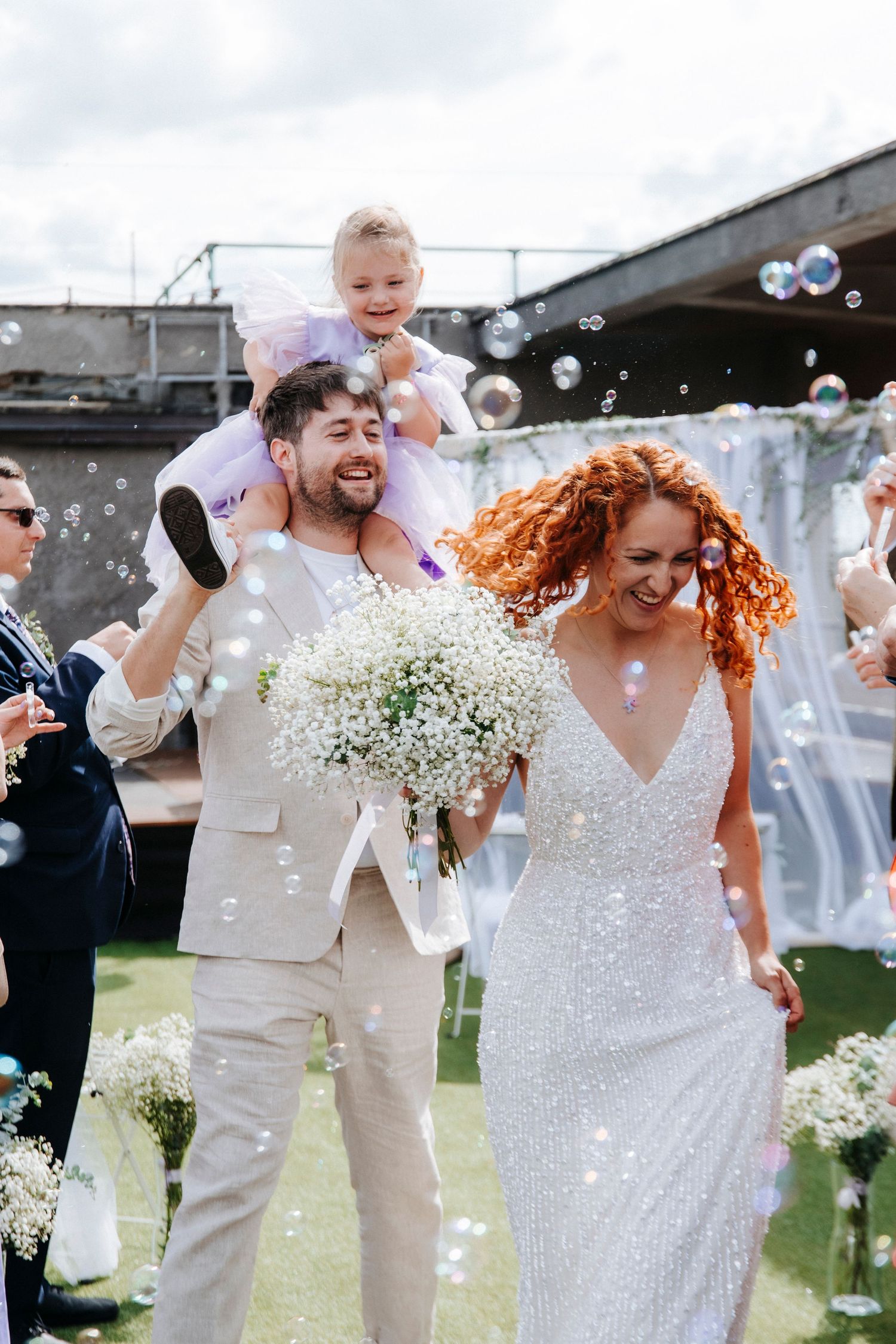 Joyful wedding celebration with bubbles and white floral bouquets on a lawn.