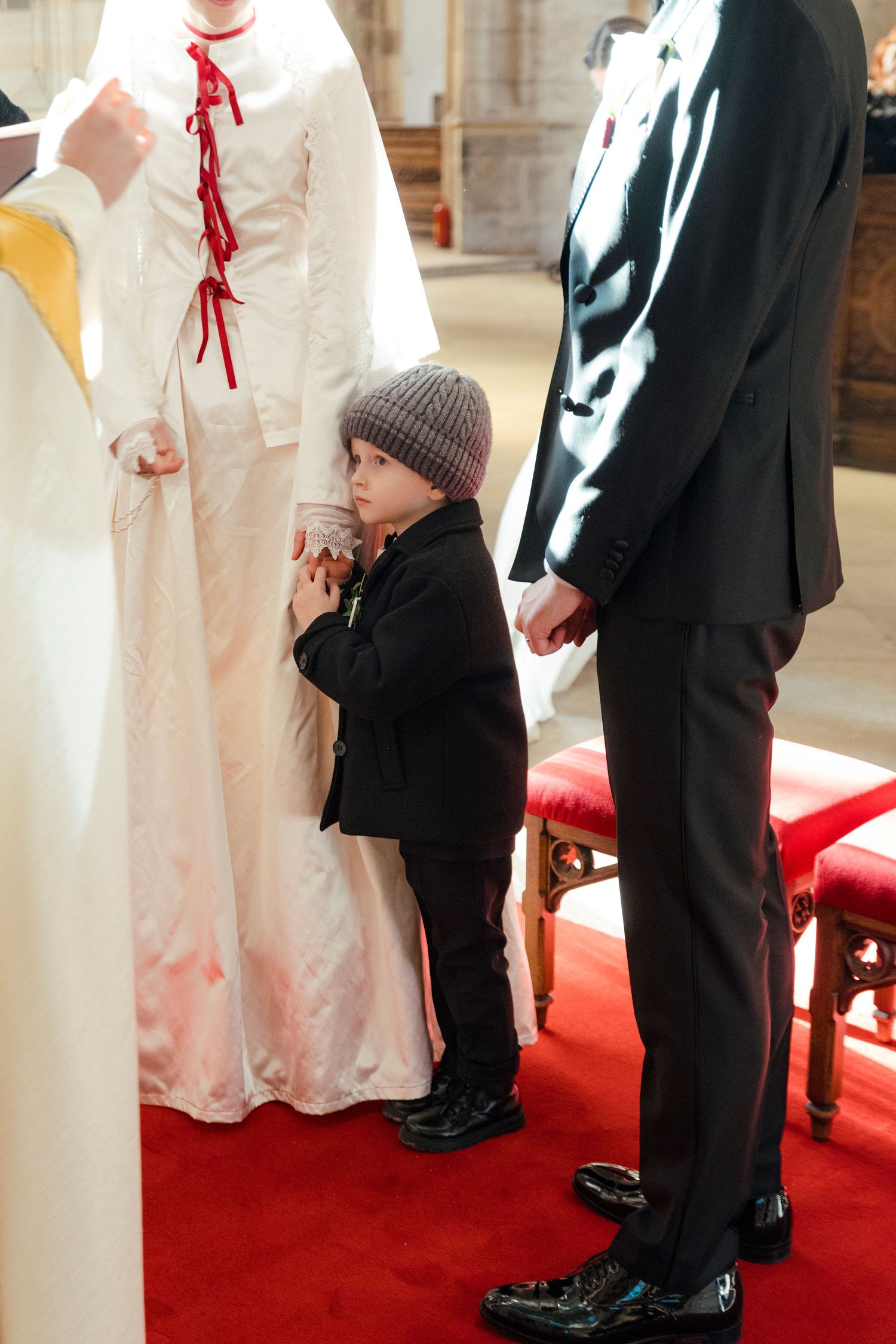 Close-up of formal shoes and dress hem on a red carpet during a wedding ceremony.