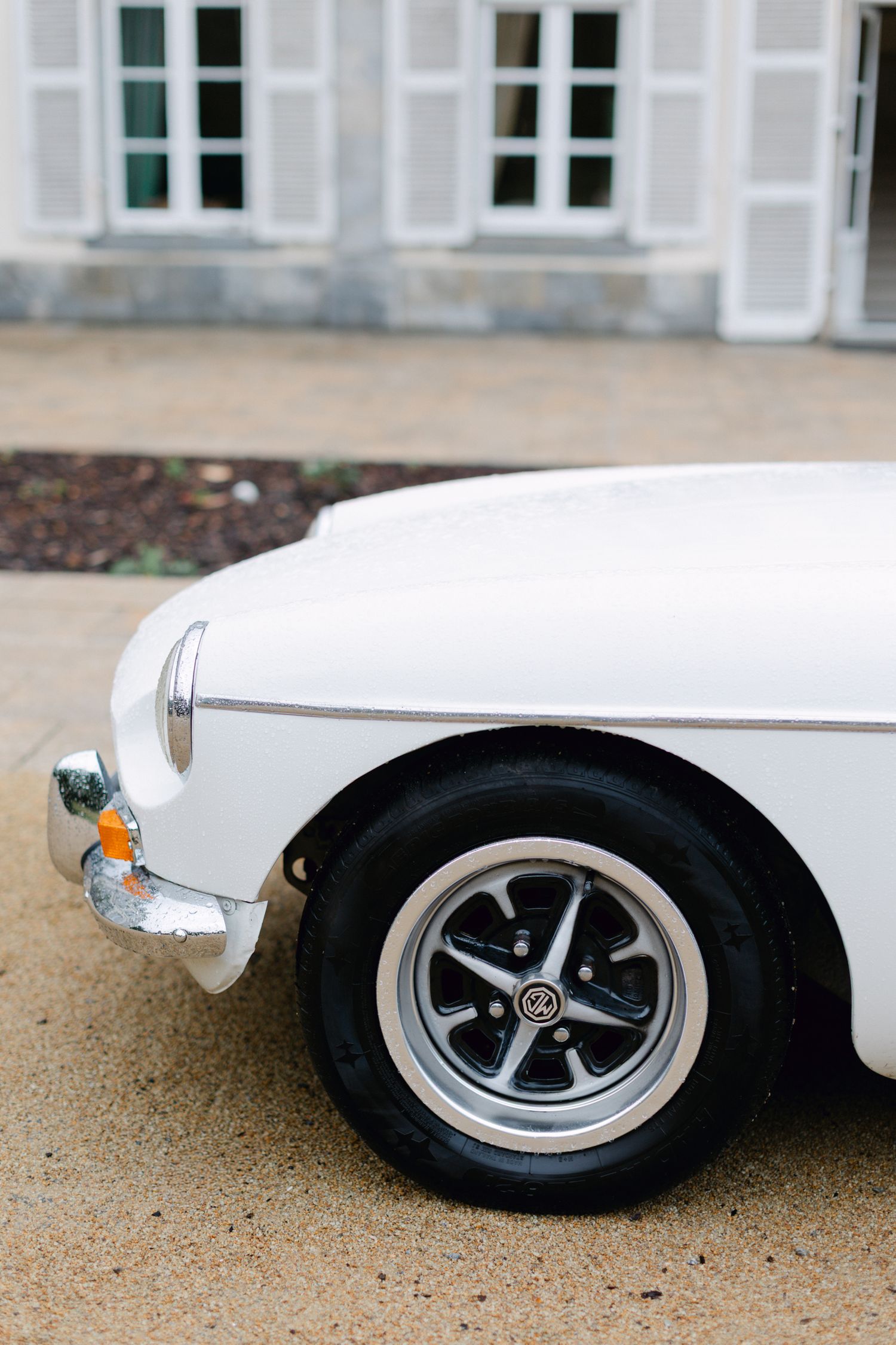 Voiture de sport vintage blanche classique garée sur une allée en gravier à l'extérieur d'un château français.