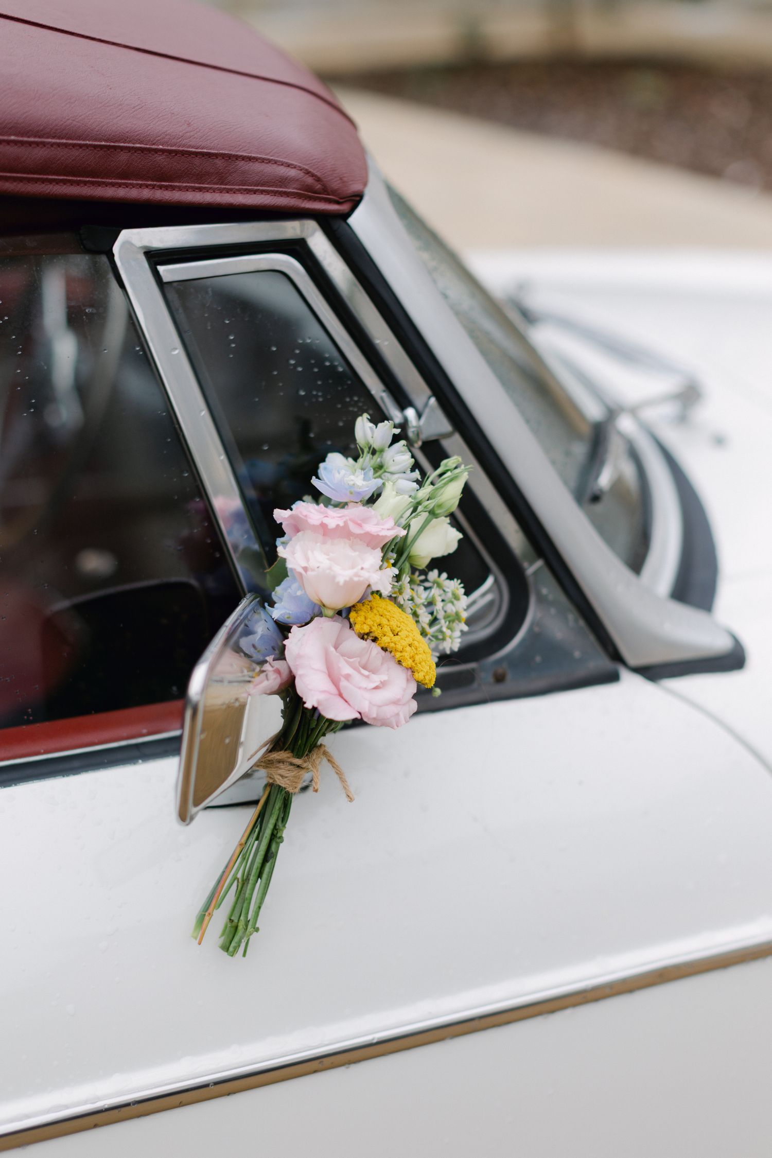 Bouquet de mariage rose et jaune attaché à un rétroviseur de voiture blanc vintage.
