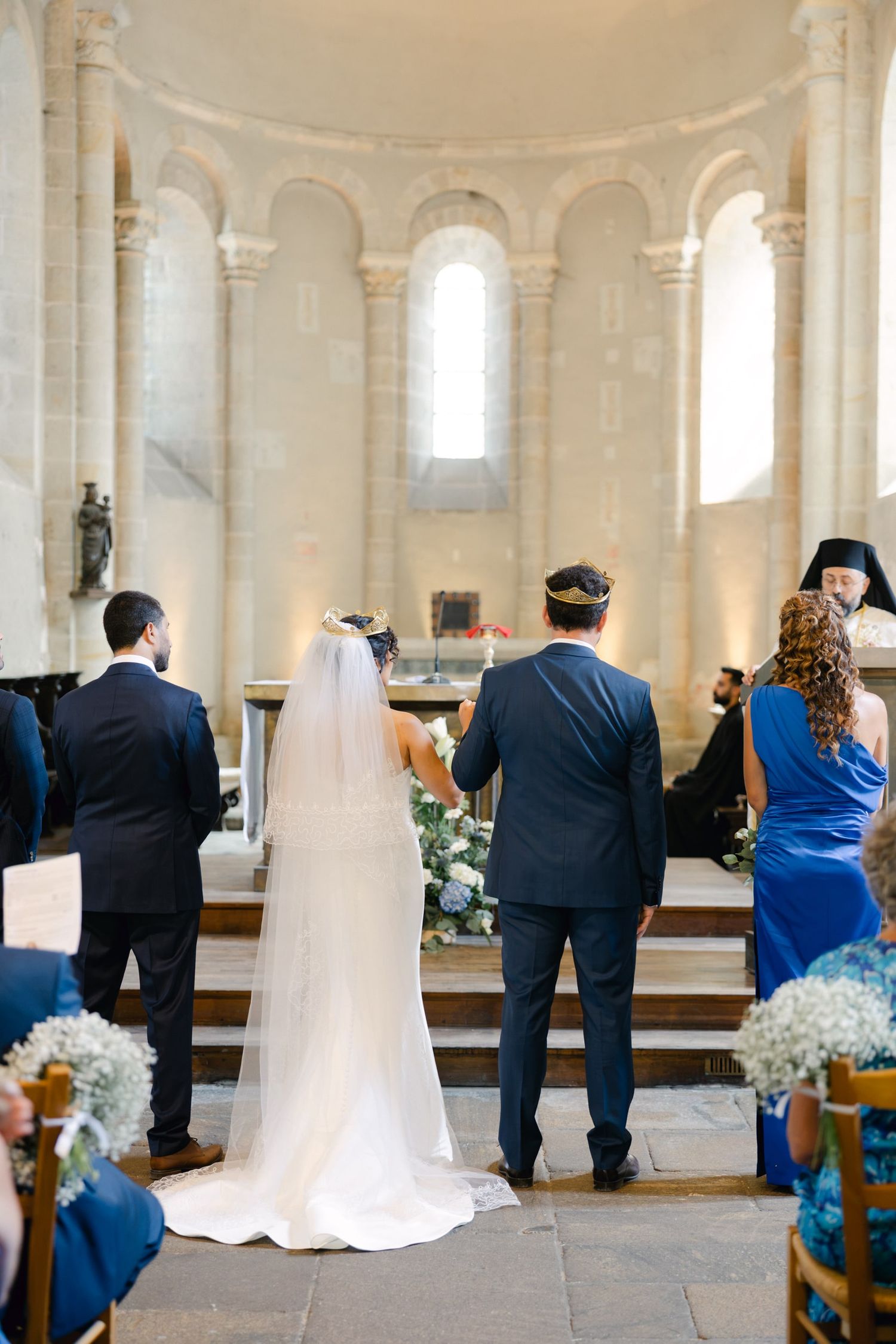 Bride and groom stand at church altar during wedding ceremony in elegant stone chapel with vaulted apse.