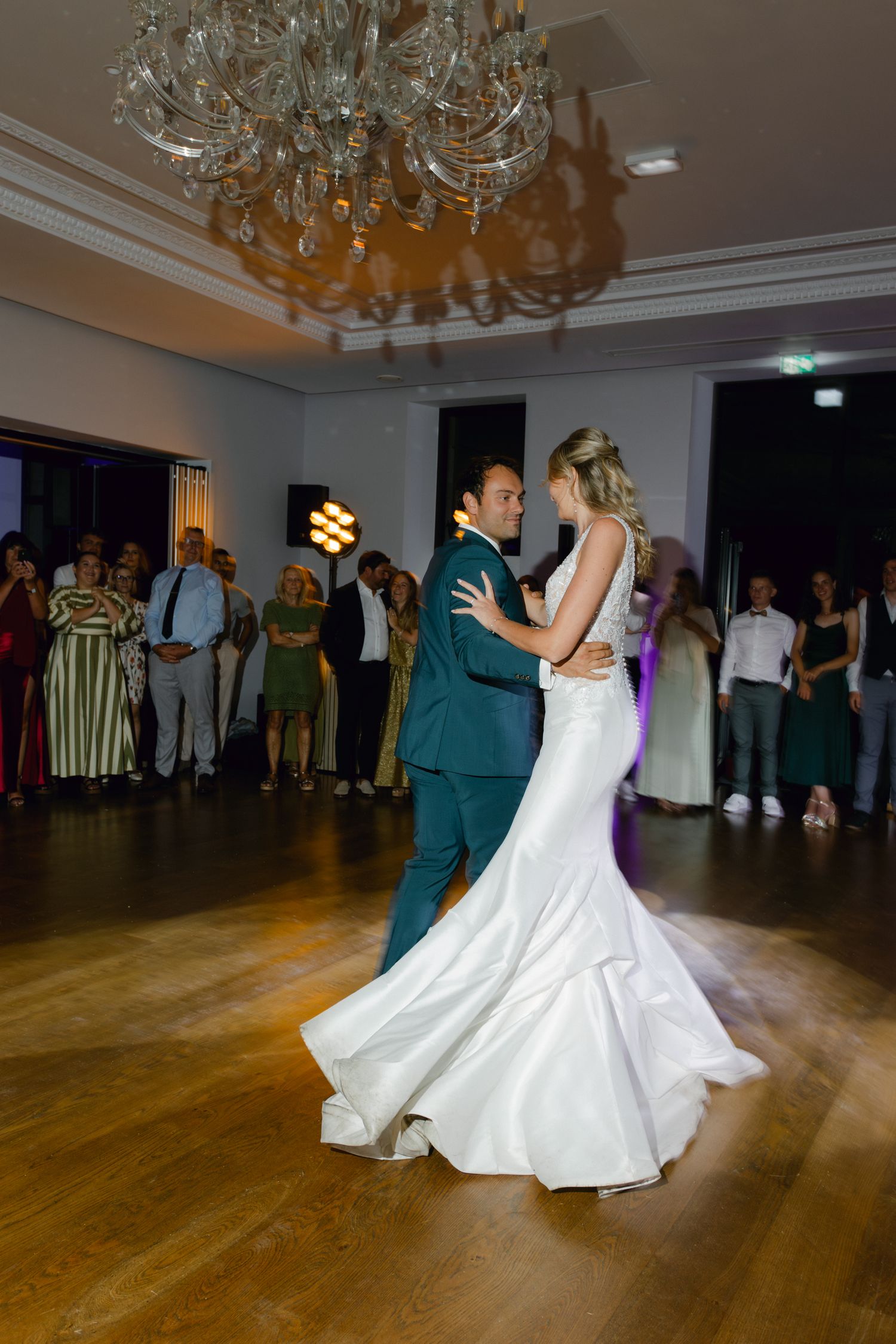 La mariée et le marié partagent leur première danse sous un lustre en cristal lors d'une élégante réception de mariage.