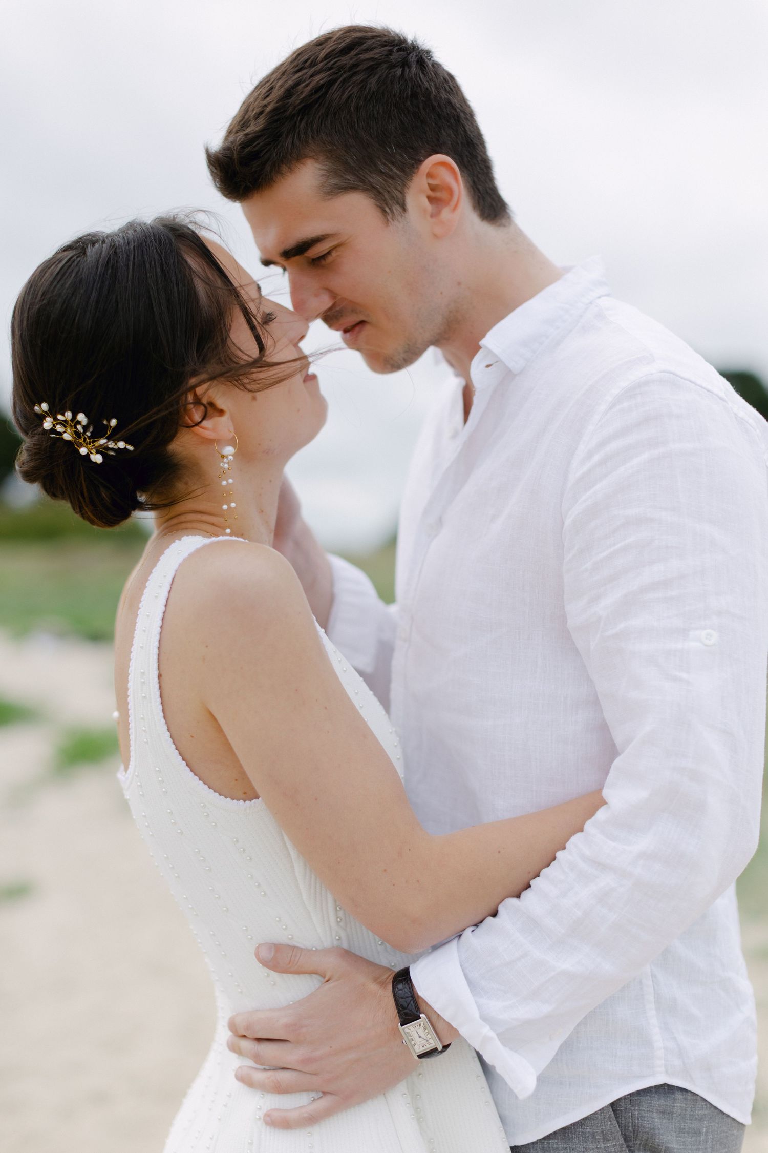 Couple romantique en tenue blanche partageant un moment intime à l'extérieur, mariée avec accessoire floral pour cheveux.