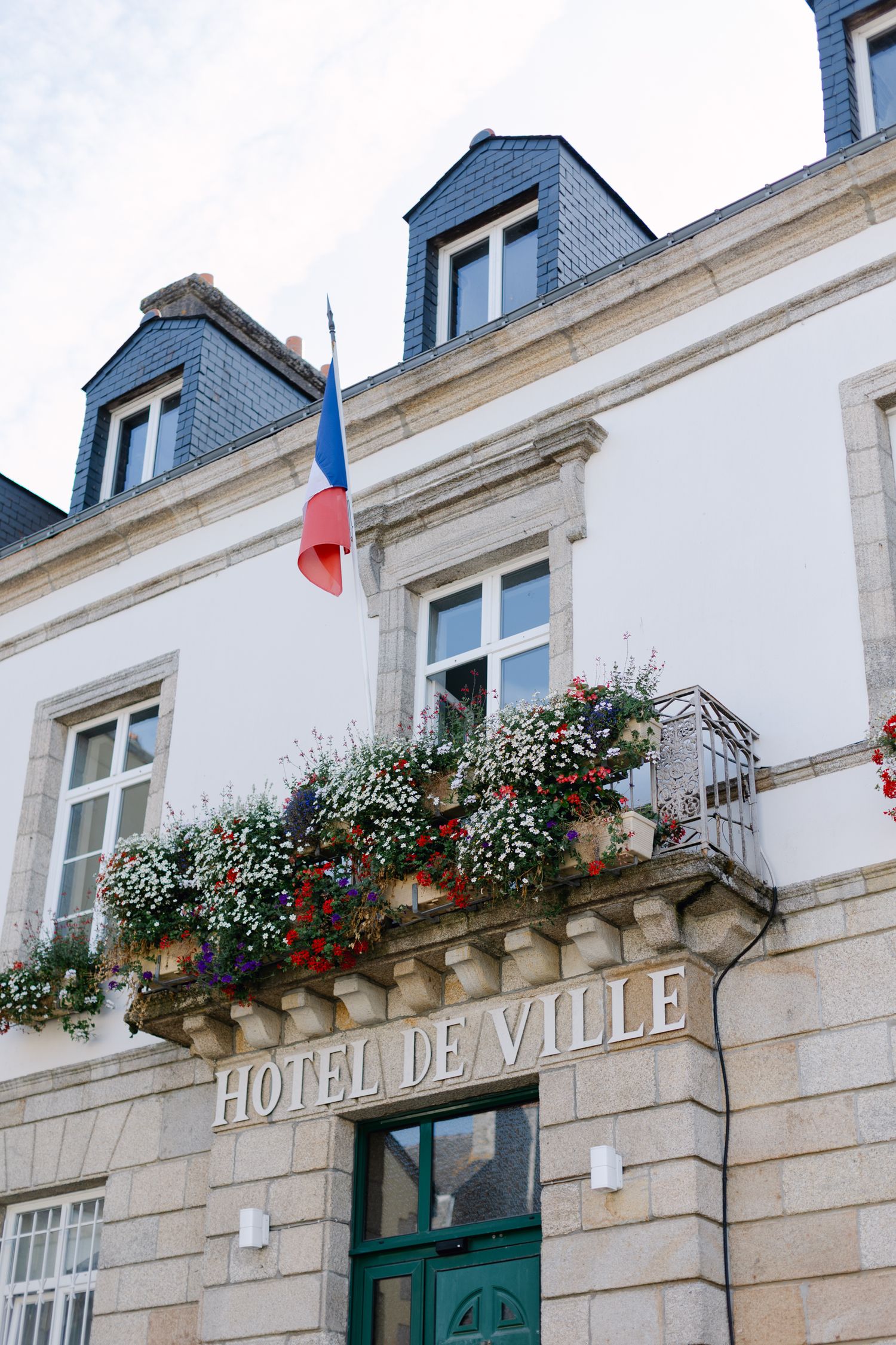 Bâtiment classique de l'hôtel de ville français avec drapeau français et décorations de balcon de fleurs colorées.
