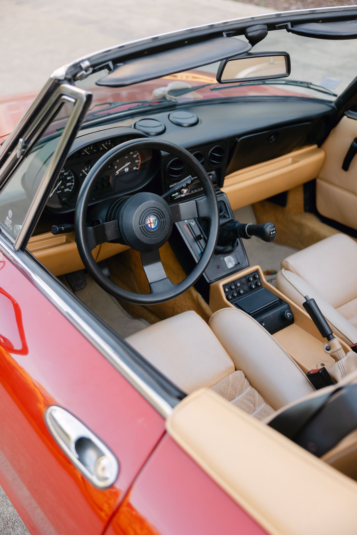Intérieur convertible Alfa Romeo rouge avec sièges en cuir beige, volant noir et commandes classiques du tableau de bord.