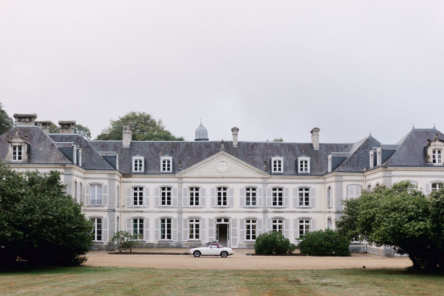 Grand lieu de mariage au château français avec pelouses soignées et architecture classique sous un ciel nuageux.