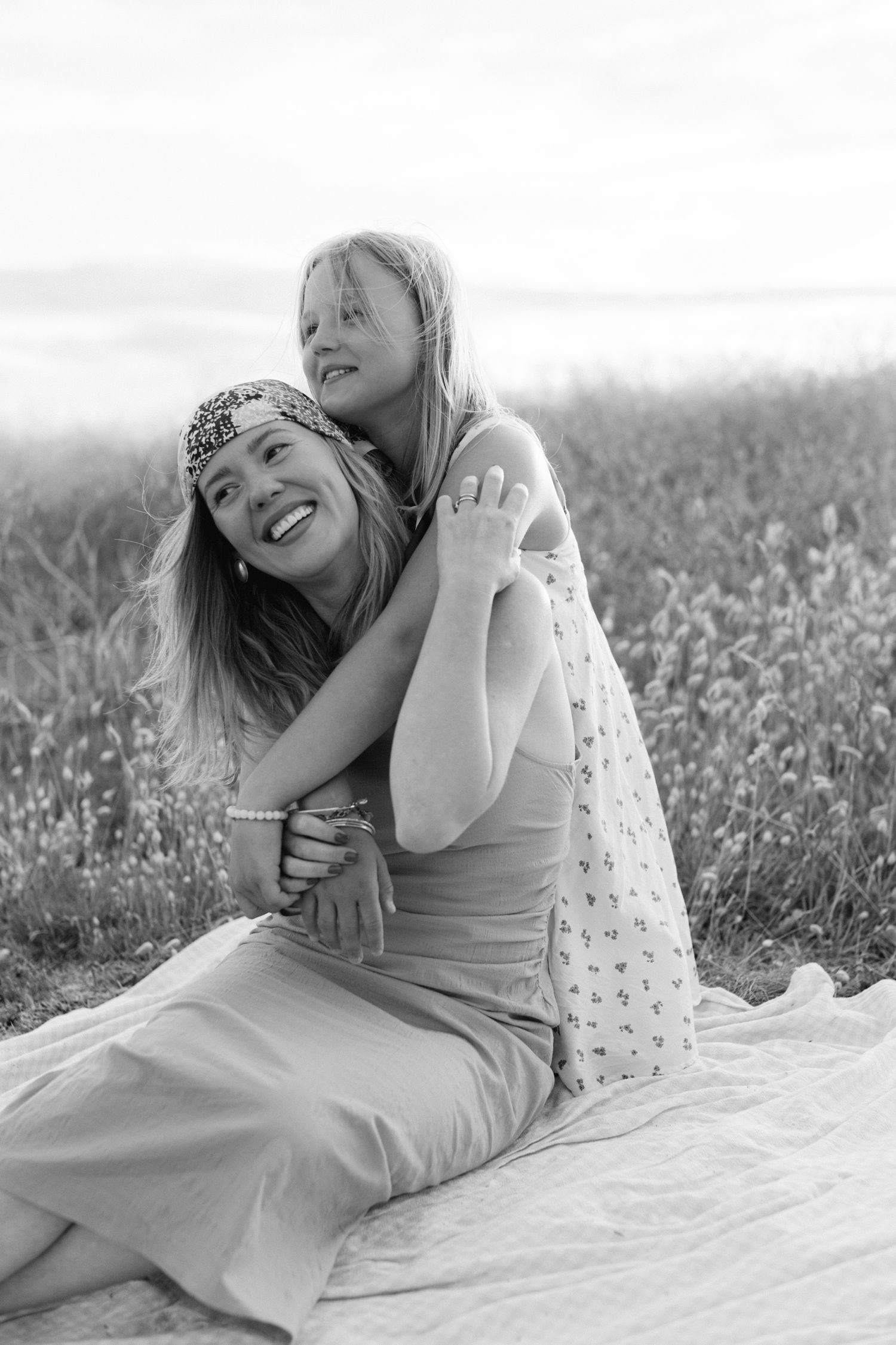 Photo en noir et blanc d'une femme et d'une jeune fille s'embrassant et riant ensemble dans un champ.